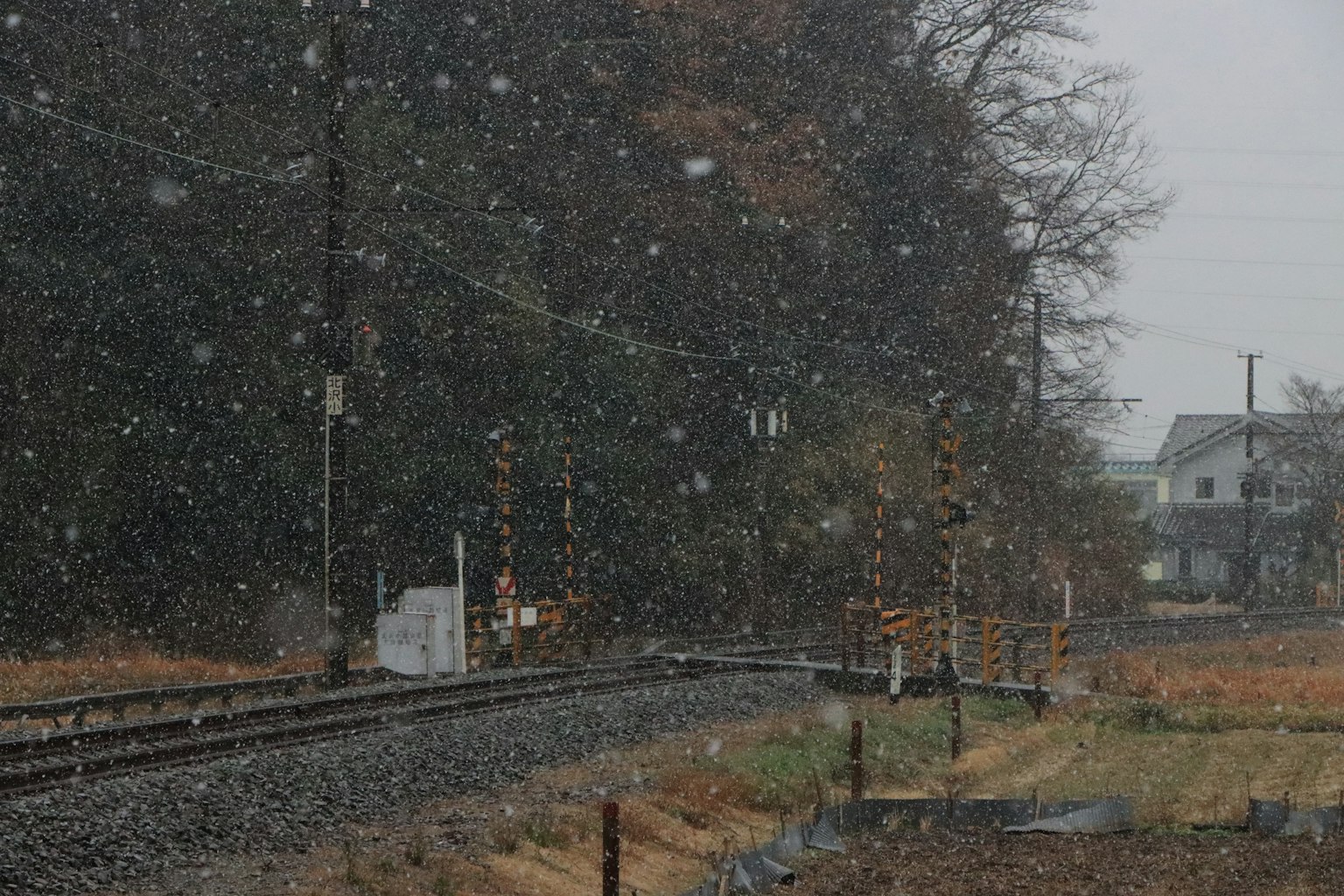 Nieve cayendo sobre una vía de tren con casas cercanas