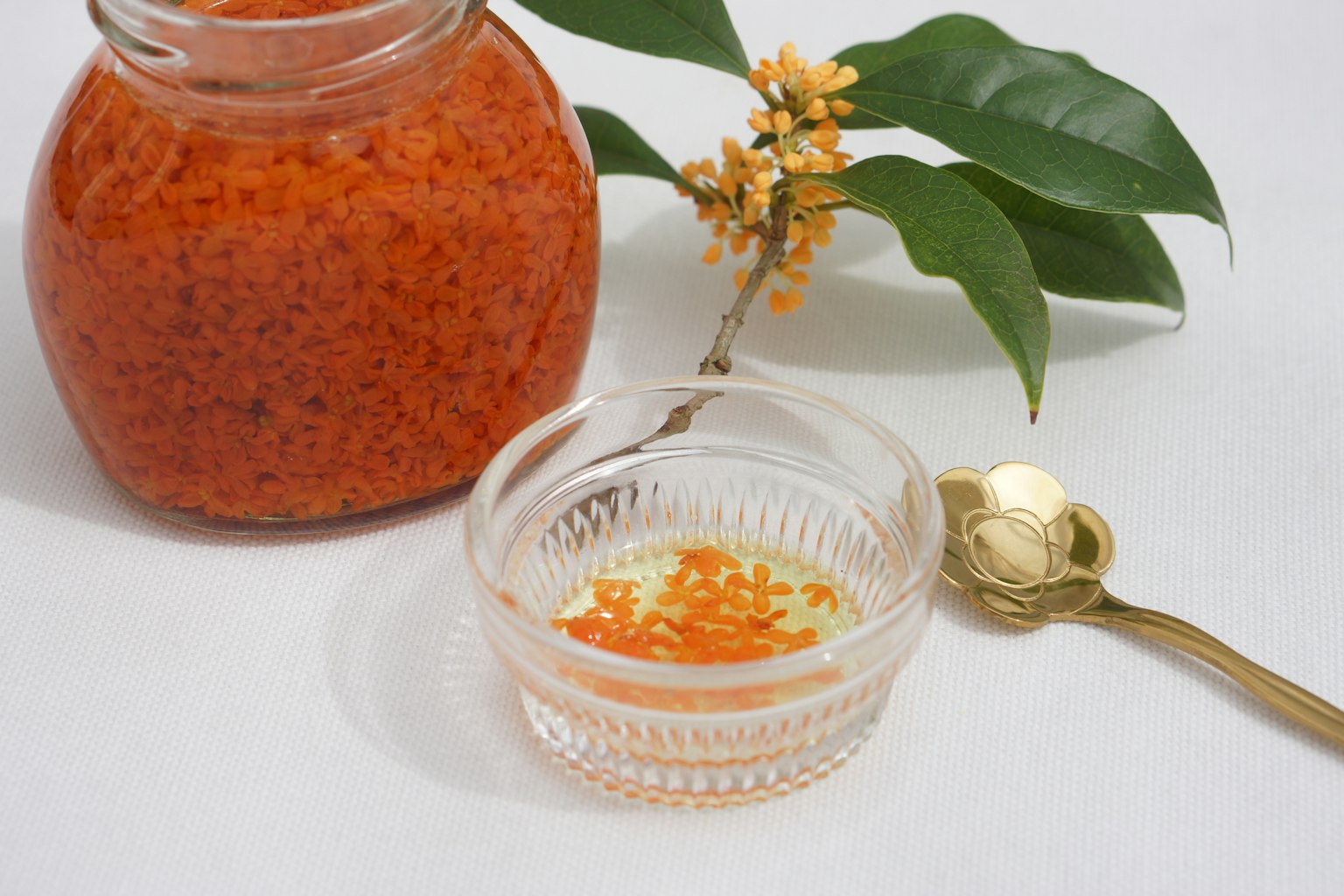 Un frasco de condimento naranja vibrante junto a un platillo pequeño con condimento y una hoja decorativa y una flor