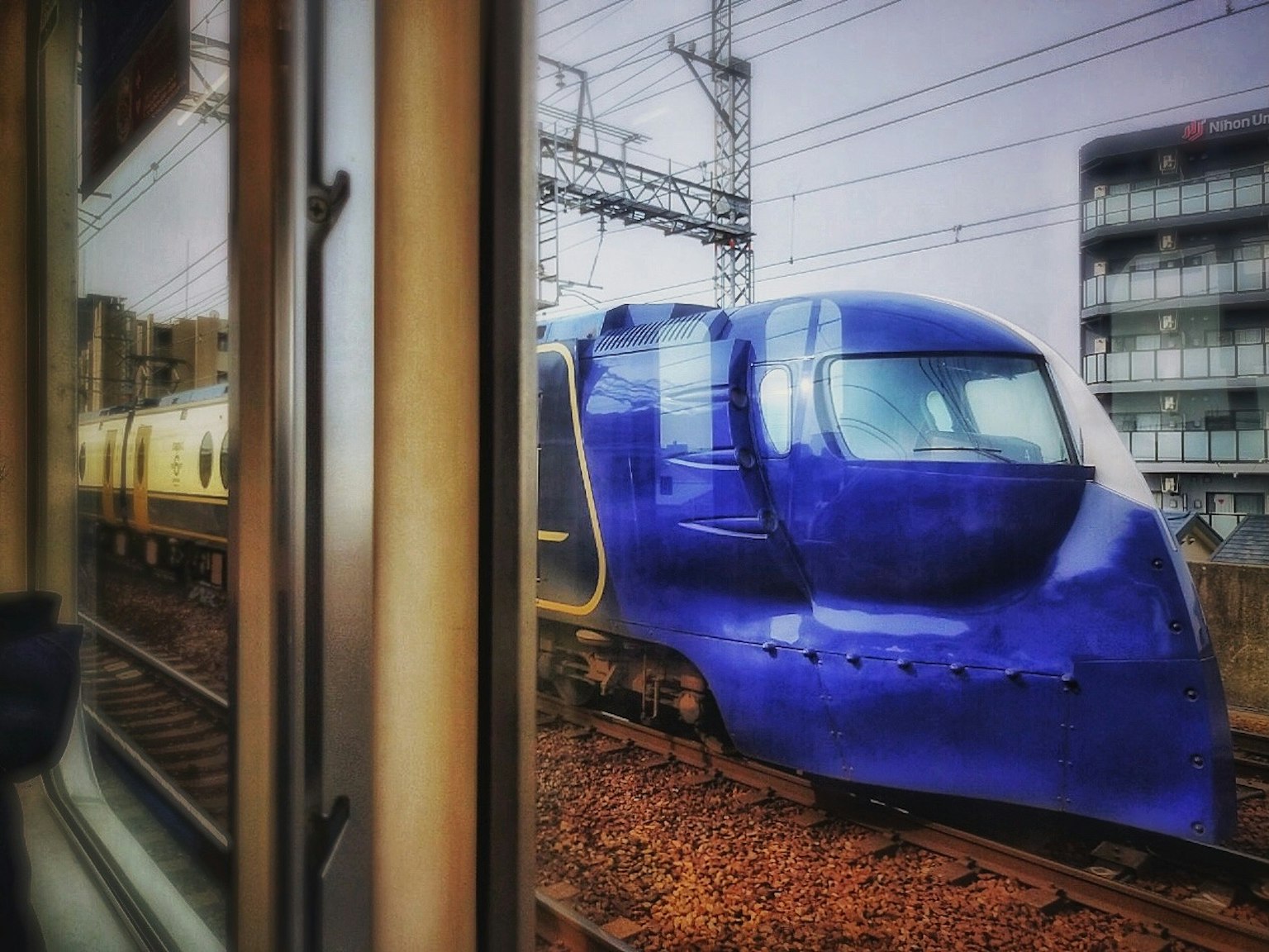รถไฟสีน้ำเงินจอดอยู่ข้างทางรถไฟมีอาคารอยู่เบื้องหลัง