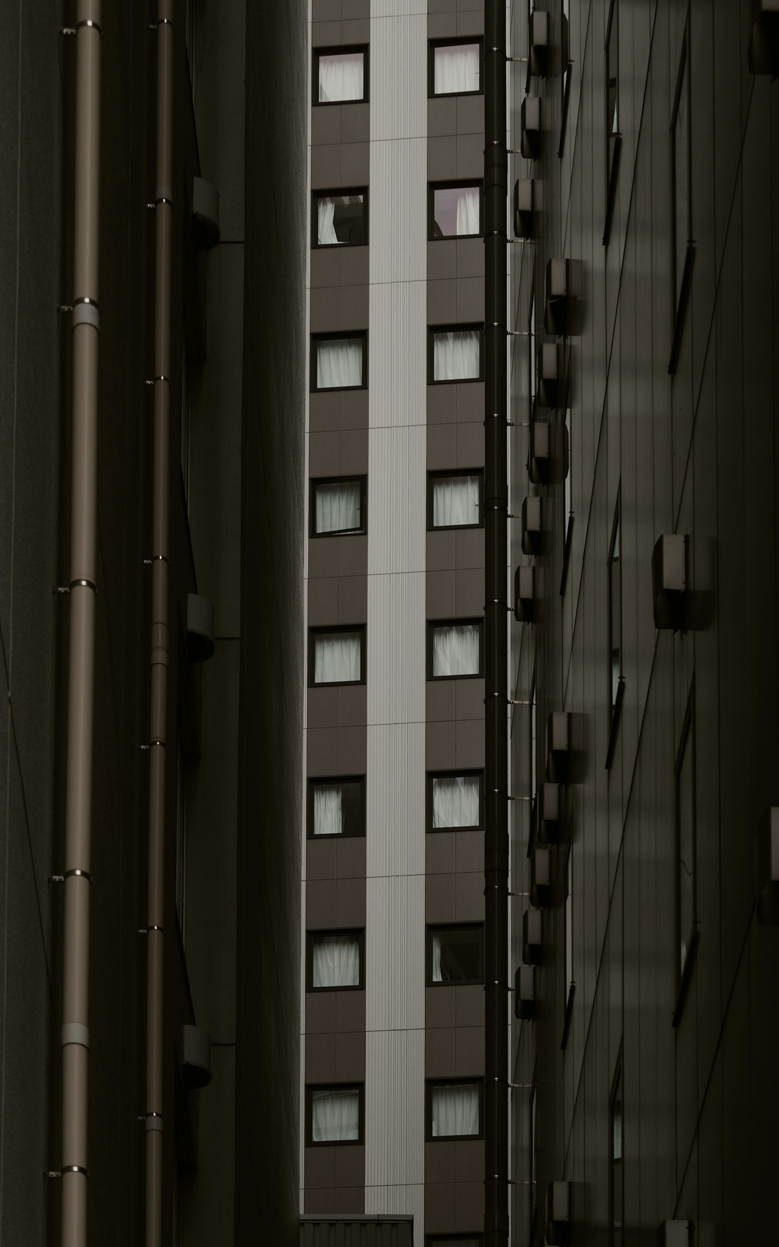 Exterior view of a building along a narrow passage between high-rise structures featuring a simple design with aligned windows