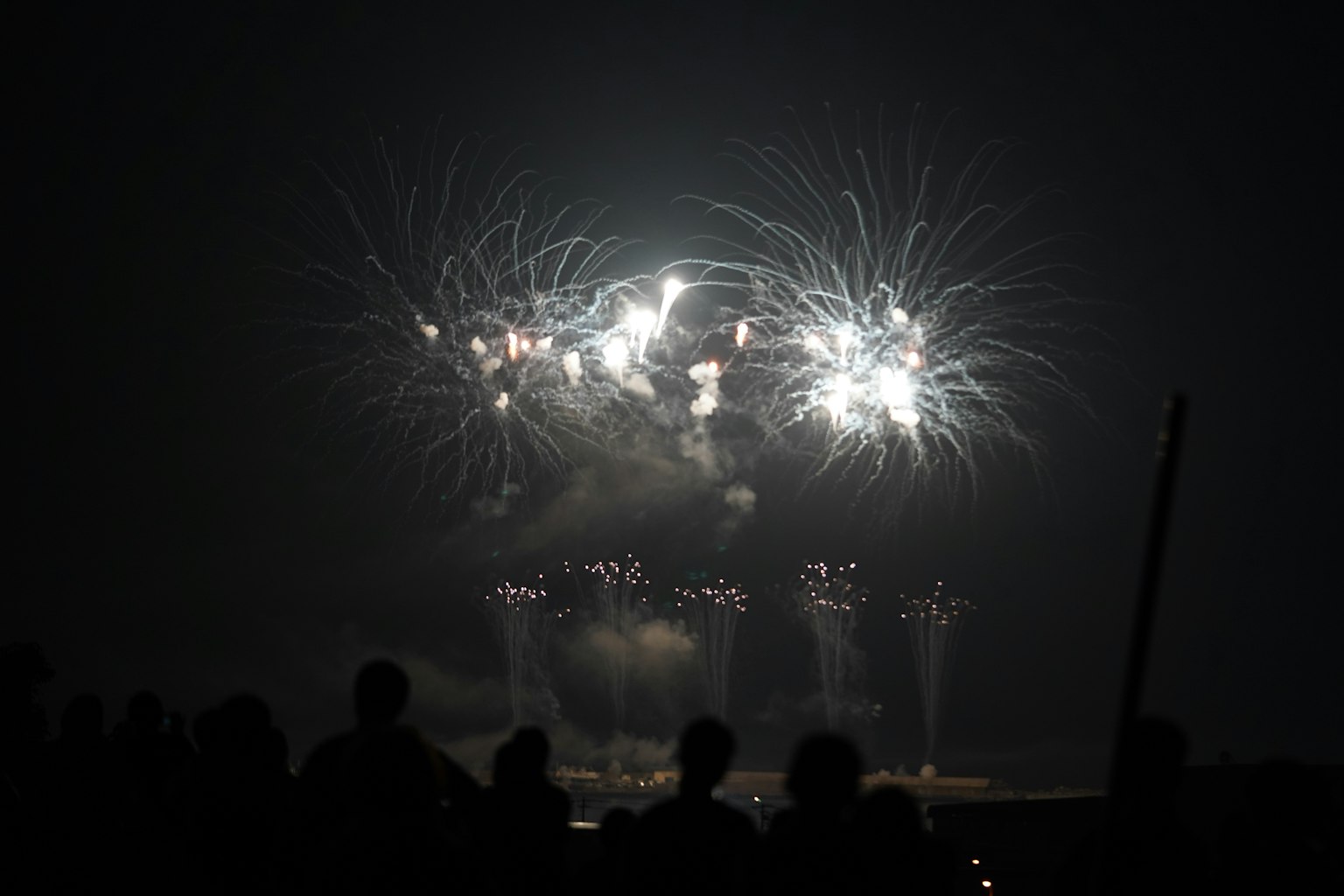 Fuegos artificiales iluminando el cielo nocturno con espectadores en silueta