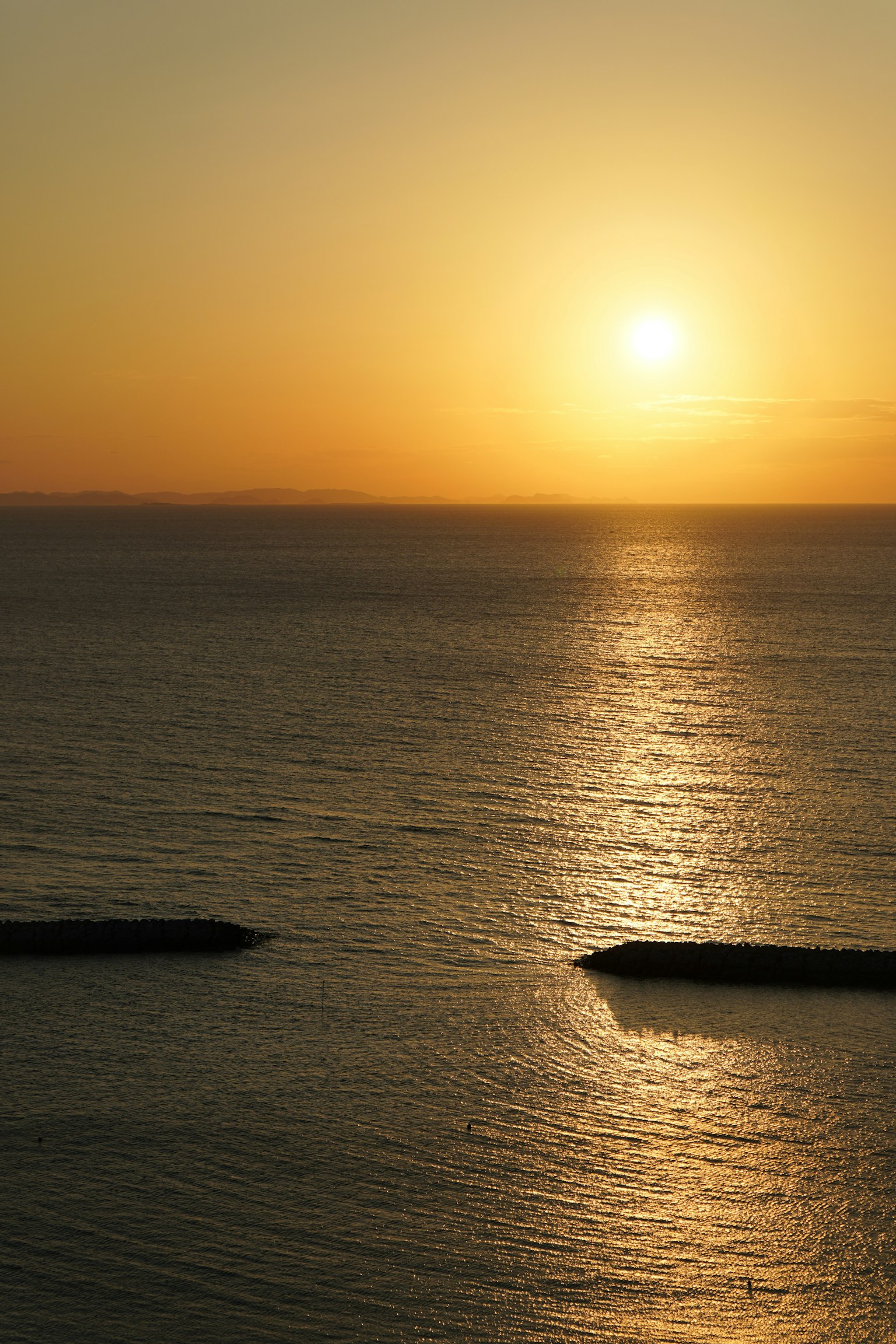 Tramonto su acque oceaniche calme con silhouette di frangiflutti