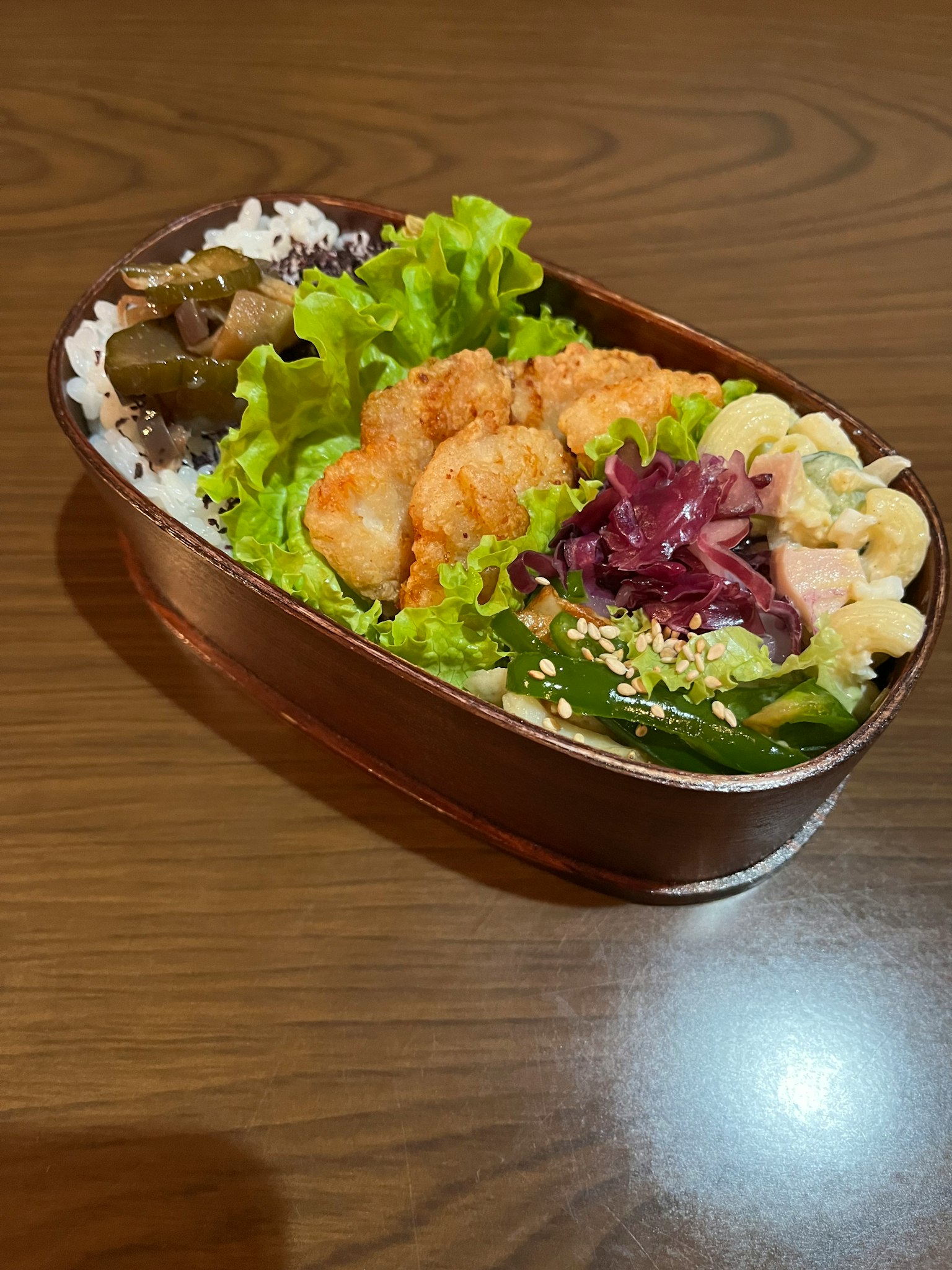 Una scatola bento riempita di riso, gamberi fritti, lattuga, banana e cavolo rosso