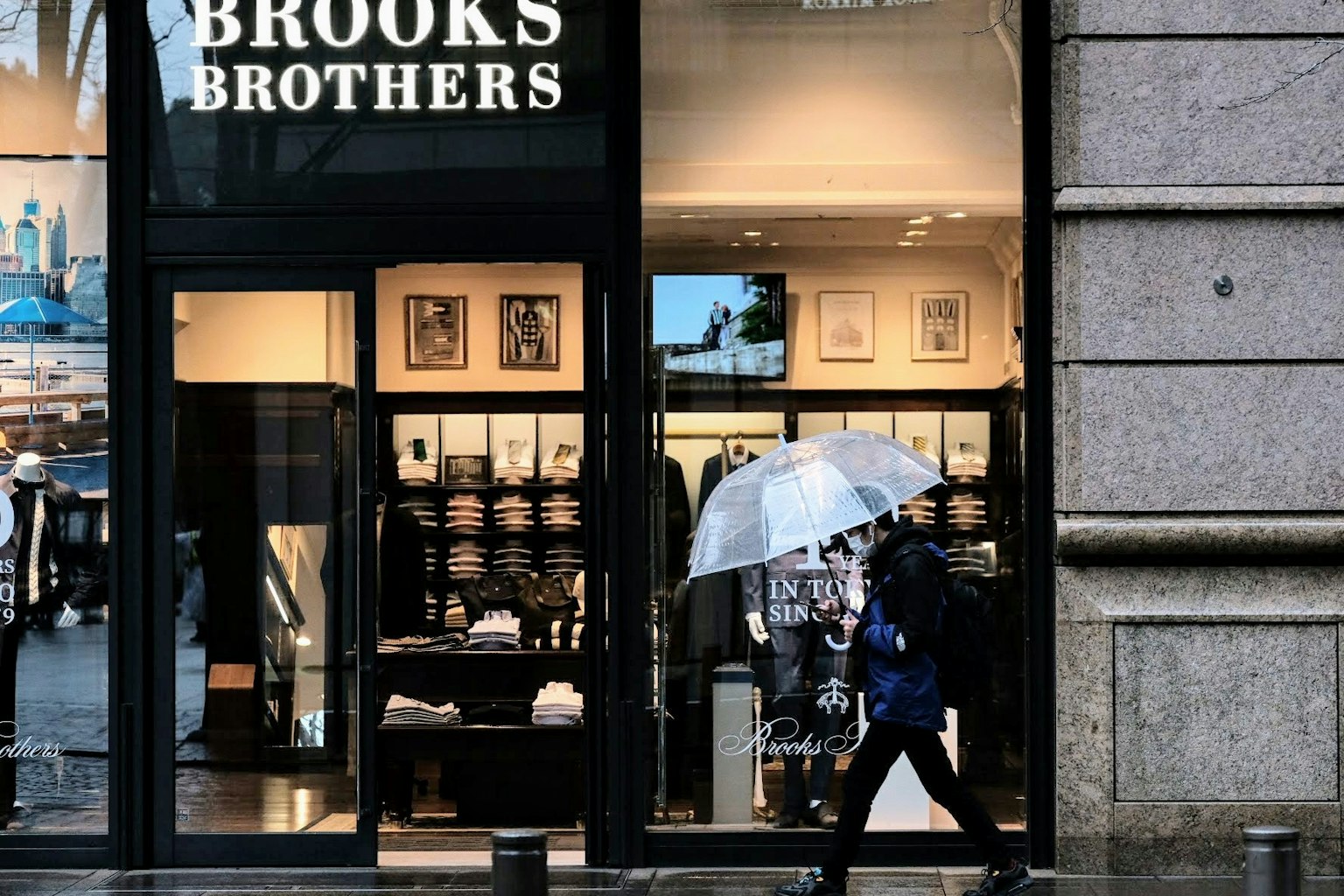 Seseorang berjalan dengan payung di depan toko Brooks Brothers