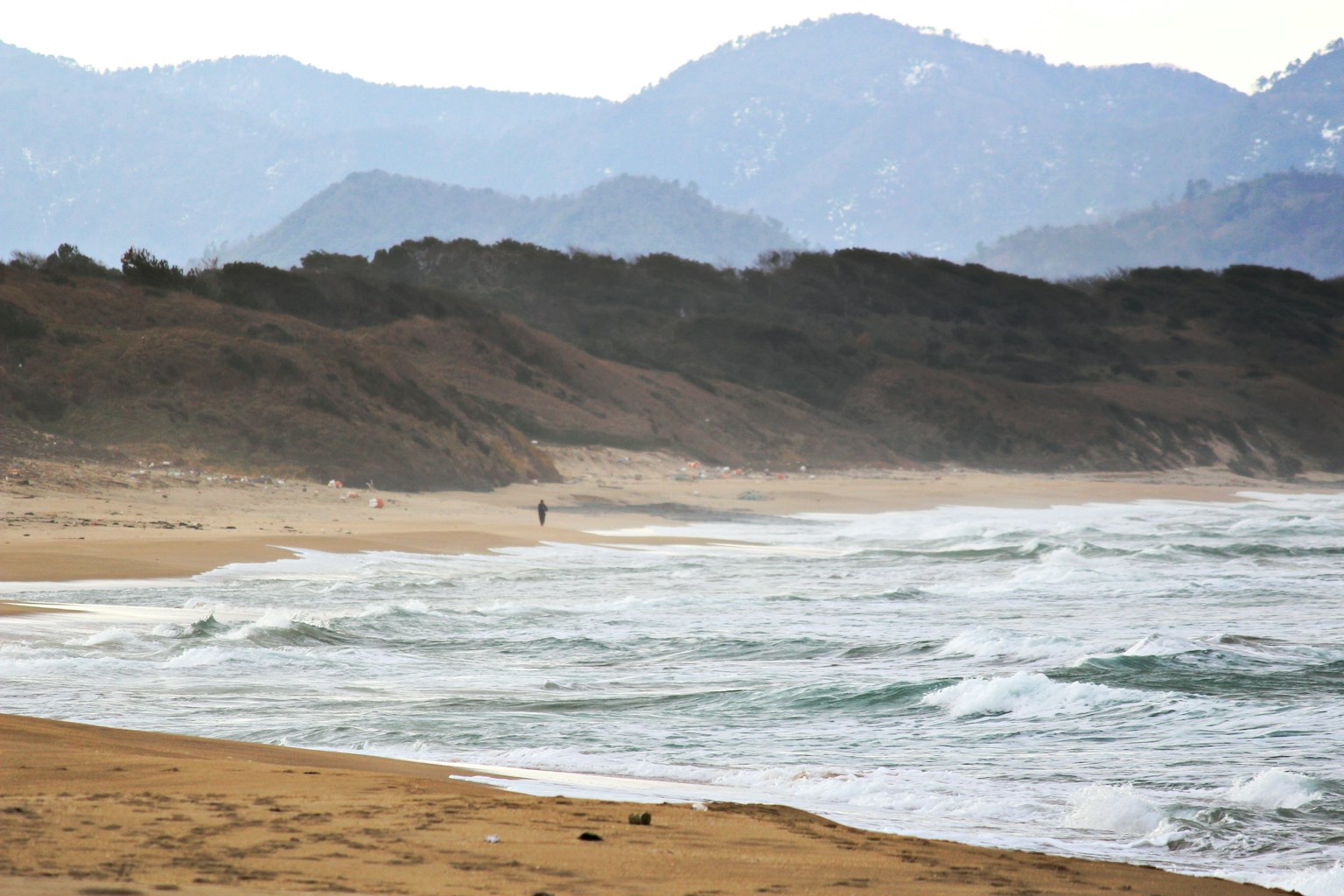 A person walking along a beach with mountains in the background