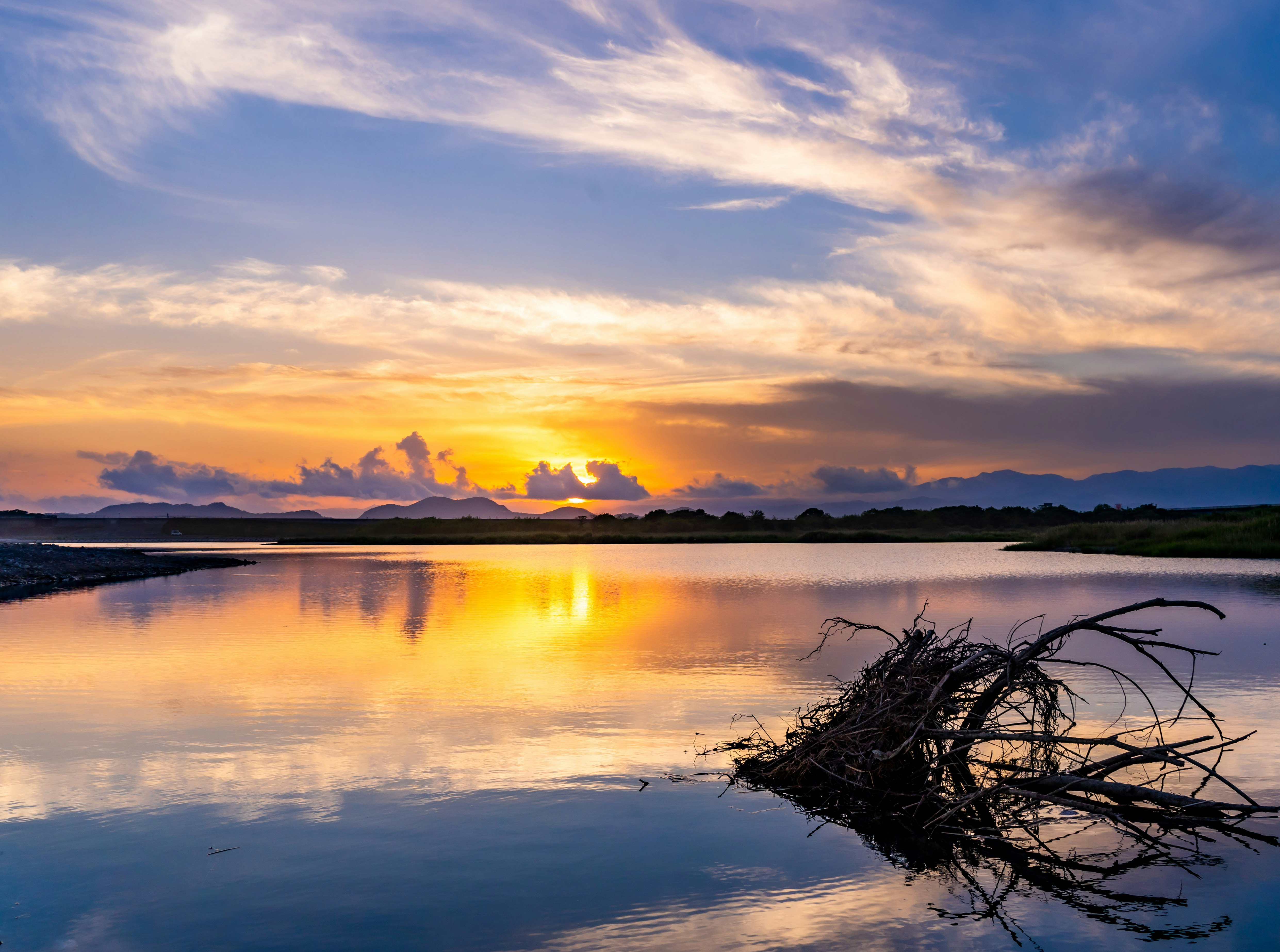sunset clouds reflected on a calm lake with driftwood on the shore