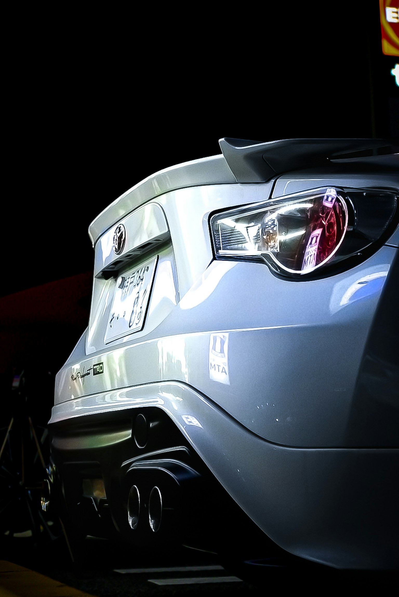Nahaufnahme des Hecks eines Sportwagens in einem Parkplatz bei Nacht mit auffälligen Rücklichtern und aerodynamischem Design