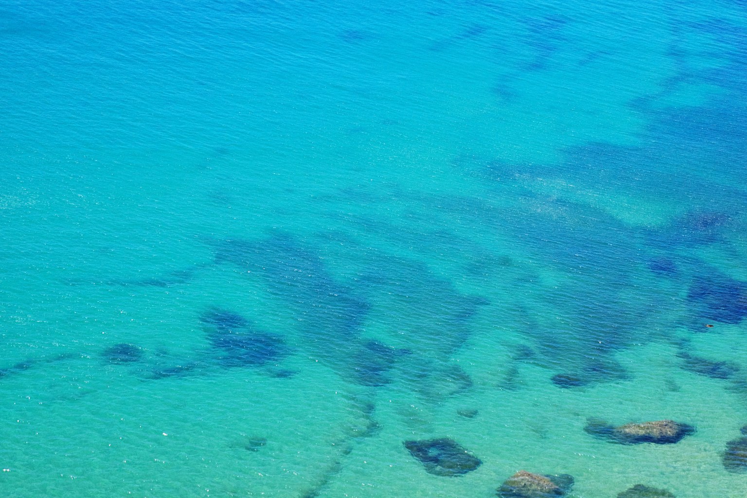 Klares blaues Wasser, das Felsen und Sandmuster darunter zeigt