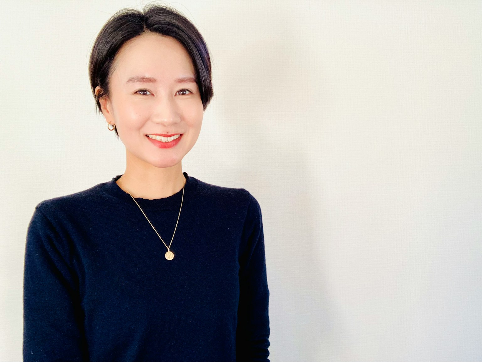 微笑女性的肖像，穿著黑色毛衣和金色項鍊，背景為白色