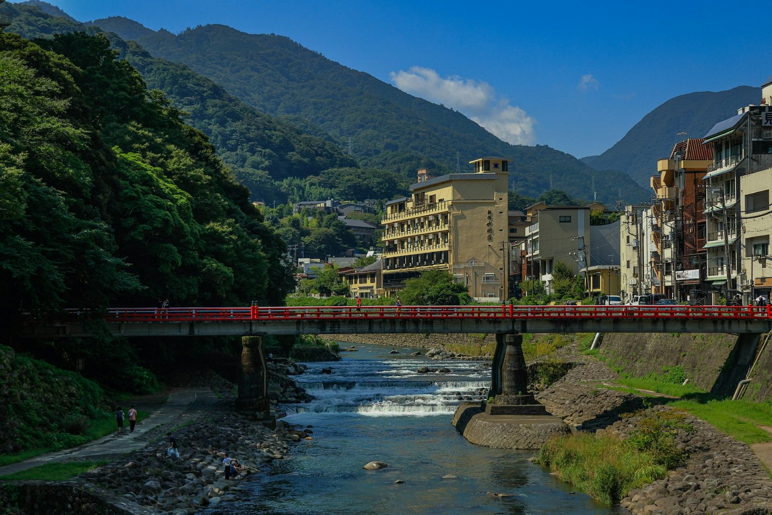 Rote Brücke, die einen Fluss überquert, mit Bergen und Gebäuden im Hintergrund