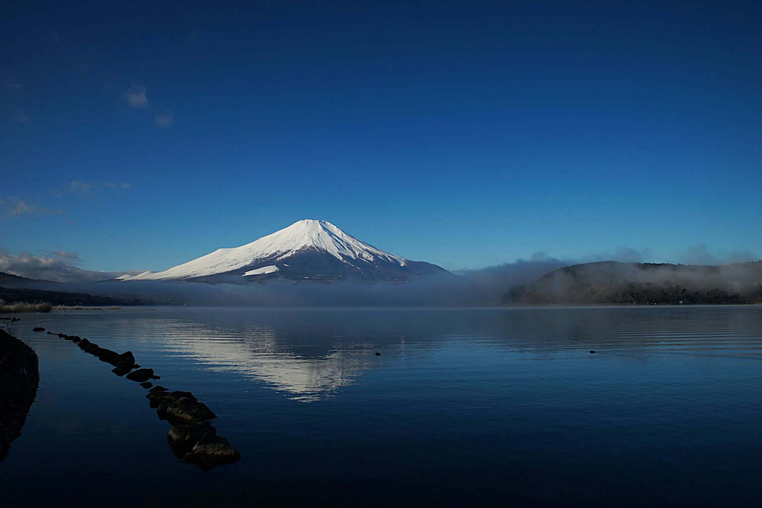 Splendido paesaggio del Monte Fuji coperto di neve che si riflette nel lago sotto un cielo blu