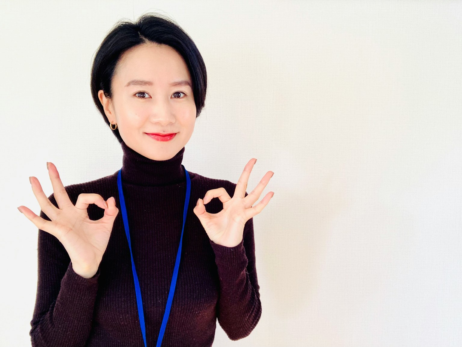 검은색 터틀넥을 입은 여성이 두 손으로 OK 사인을 만들고 있다