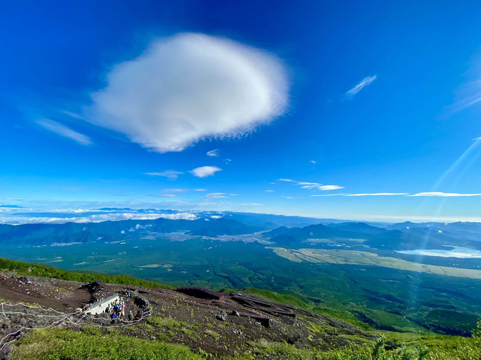 Landschaft mit Bergen und Grün unter einem blauen Himmel mit einer Wolke