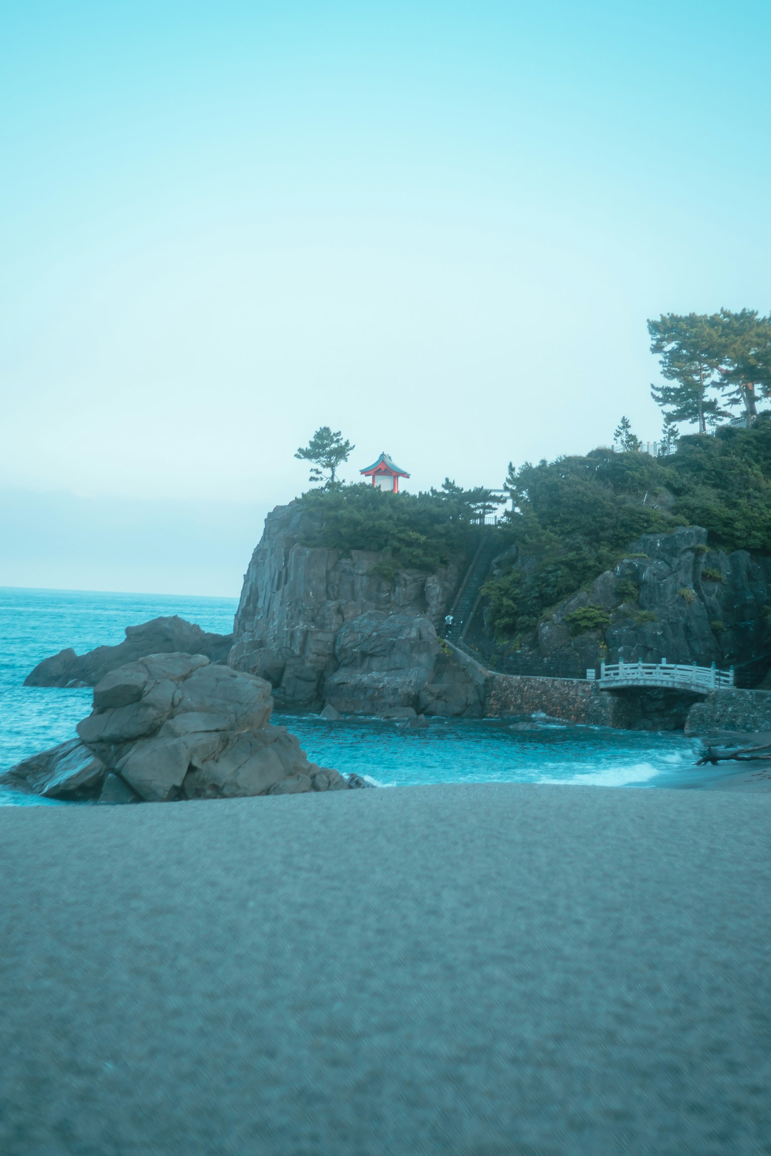 Malerscher Blick auf einen Strand mit blauem Meer und felsigen Klippen mit einem kleinen Baum