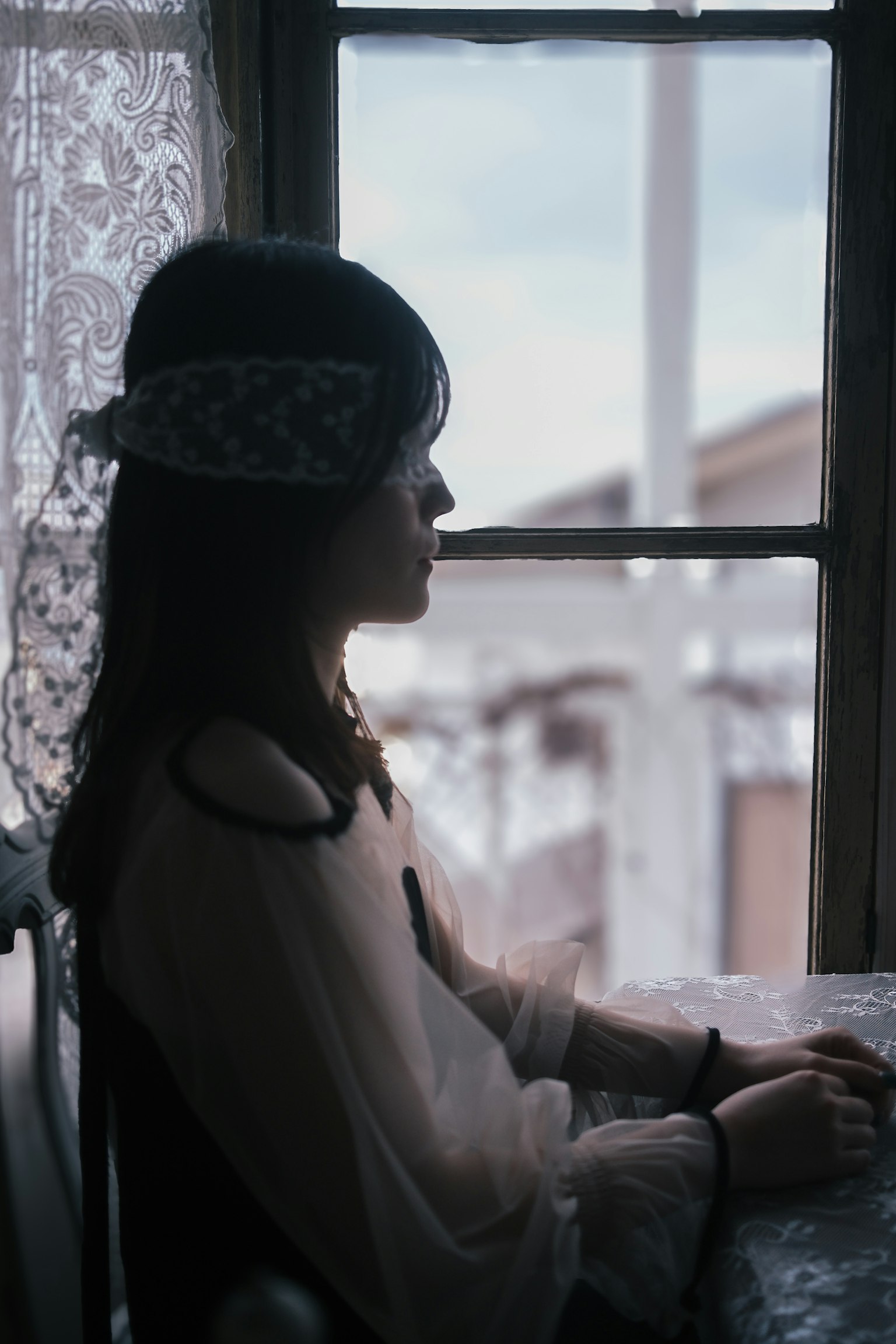 窓のそばに座る女性の横顔 繊細なレースのカーテンと薄暗い背景