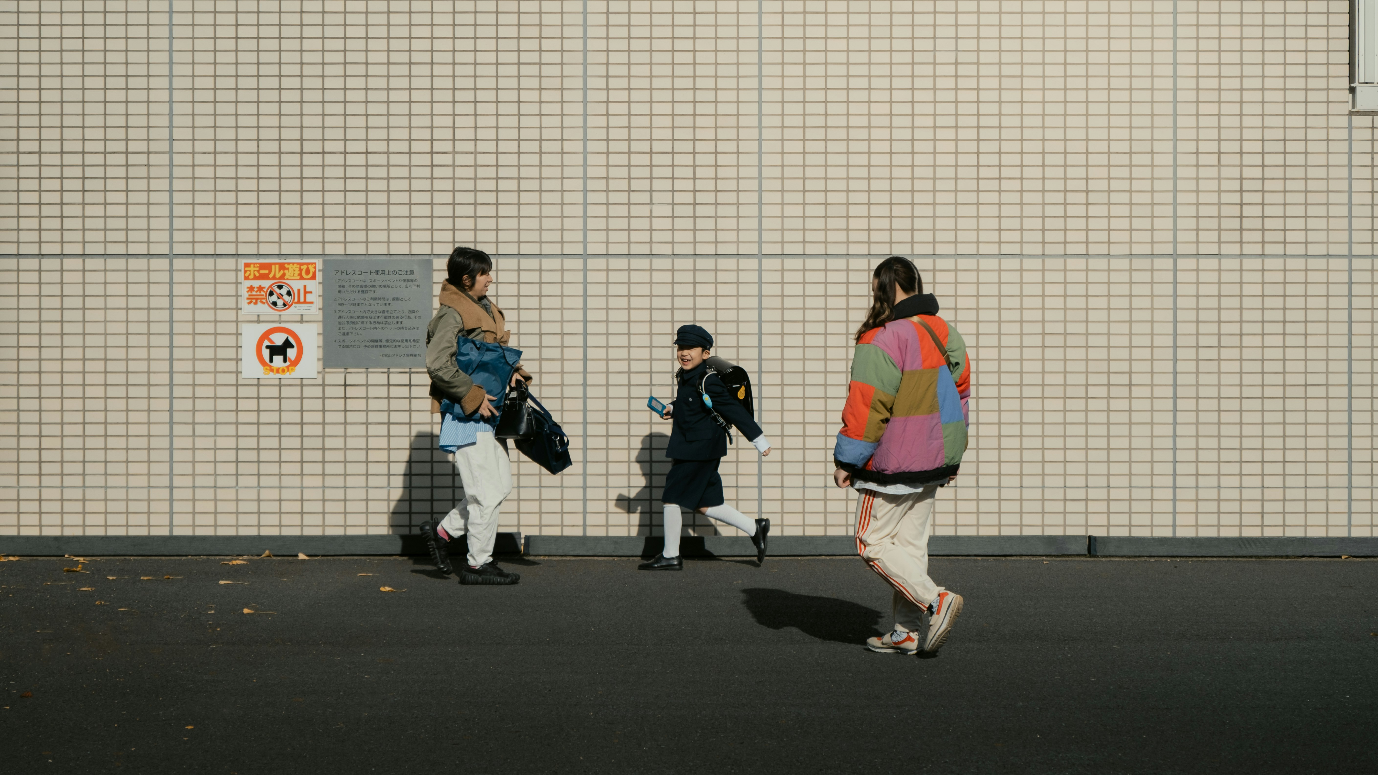 壁沿いを歩く人々とカメラを持った旅行者の後ろ姿