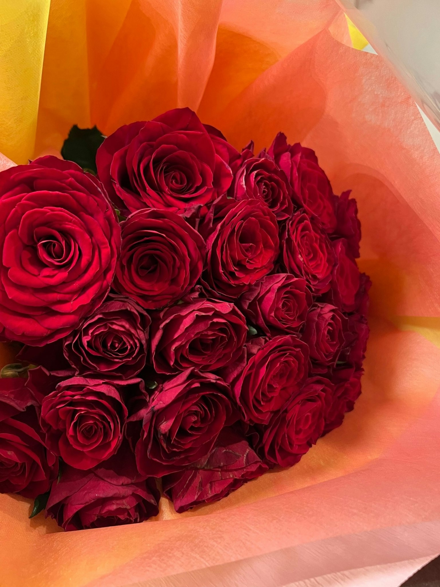 A bouquet of red roses wrapped in orange tissue paper