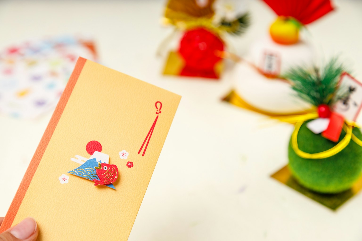 Une main tenant une enveloppe jaune avec un design du Mont Fuji et une fleur rouge