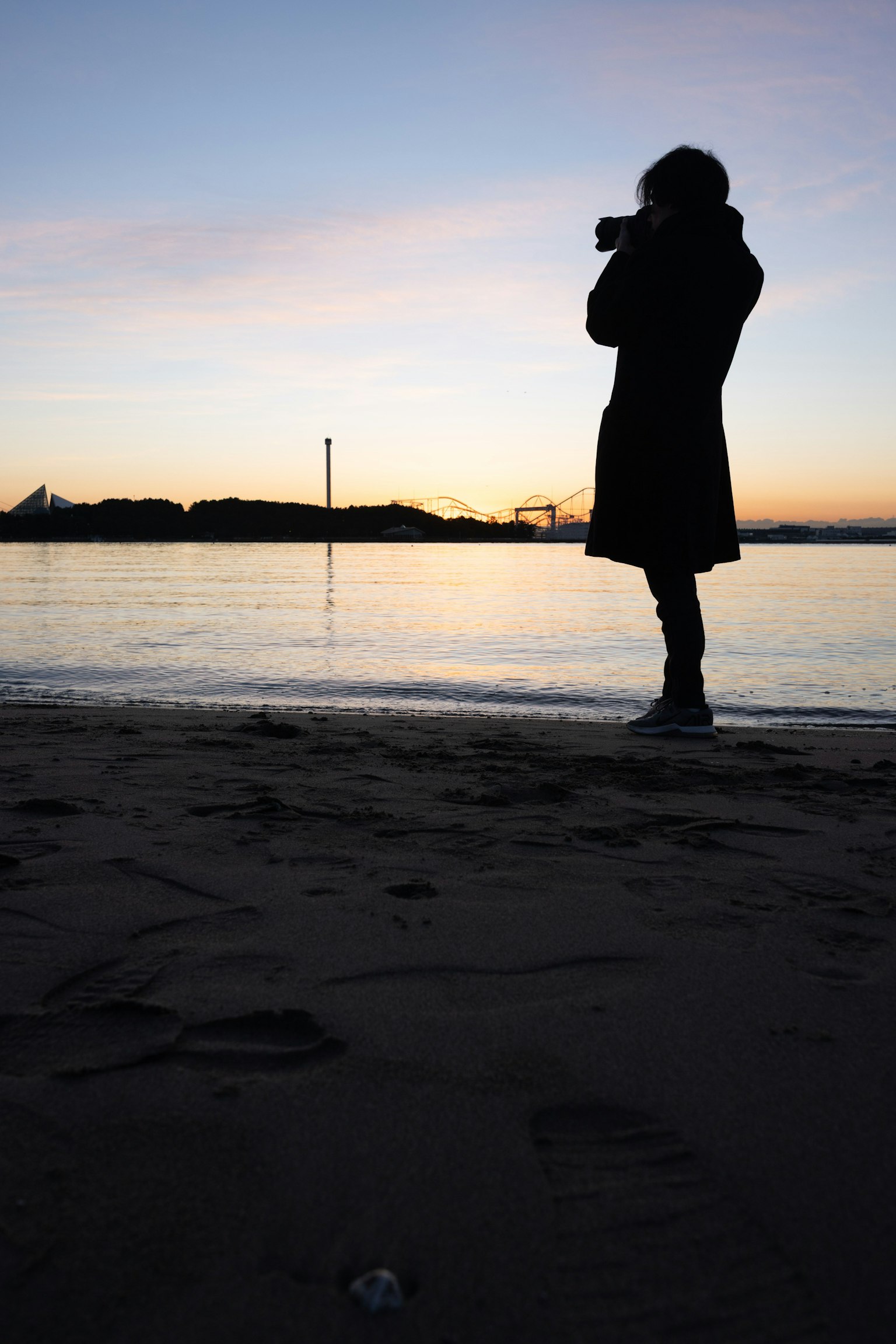 Silueta de una persona sosteniendo una cámara en la playa durante el atardecer
