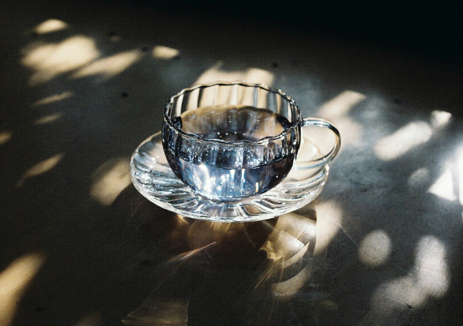 Une tasse en verre transparent avec une soucoupe posée sur une table