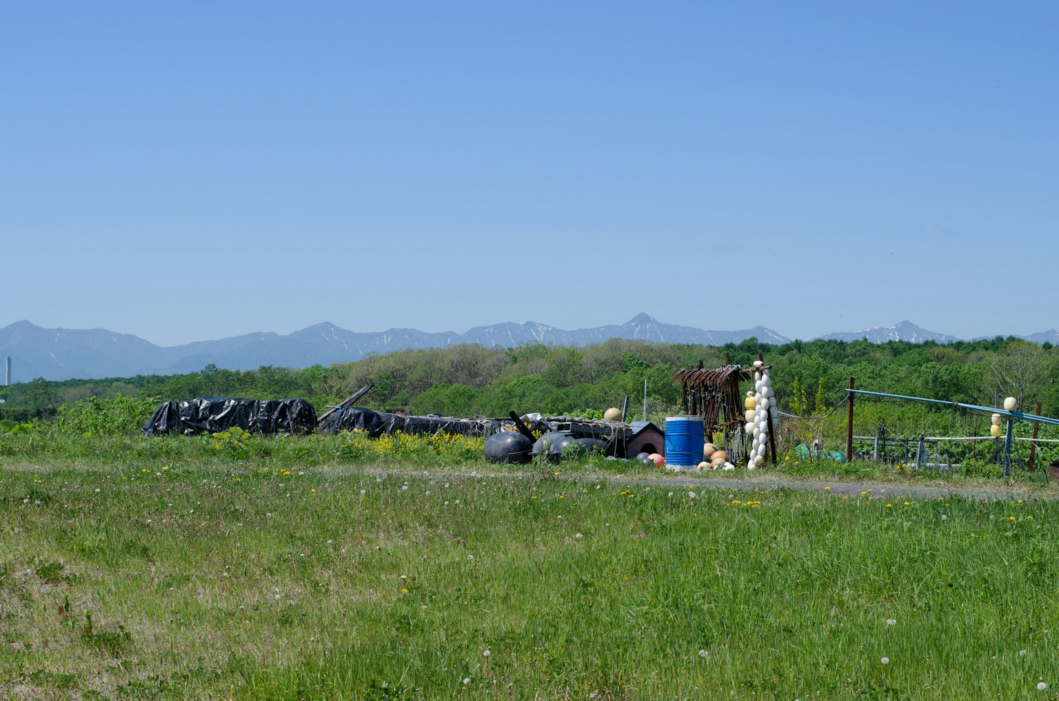 Green grassy area with a fence and trash bags against a backdrop of blue sky and mountains