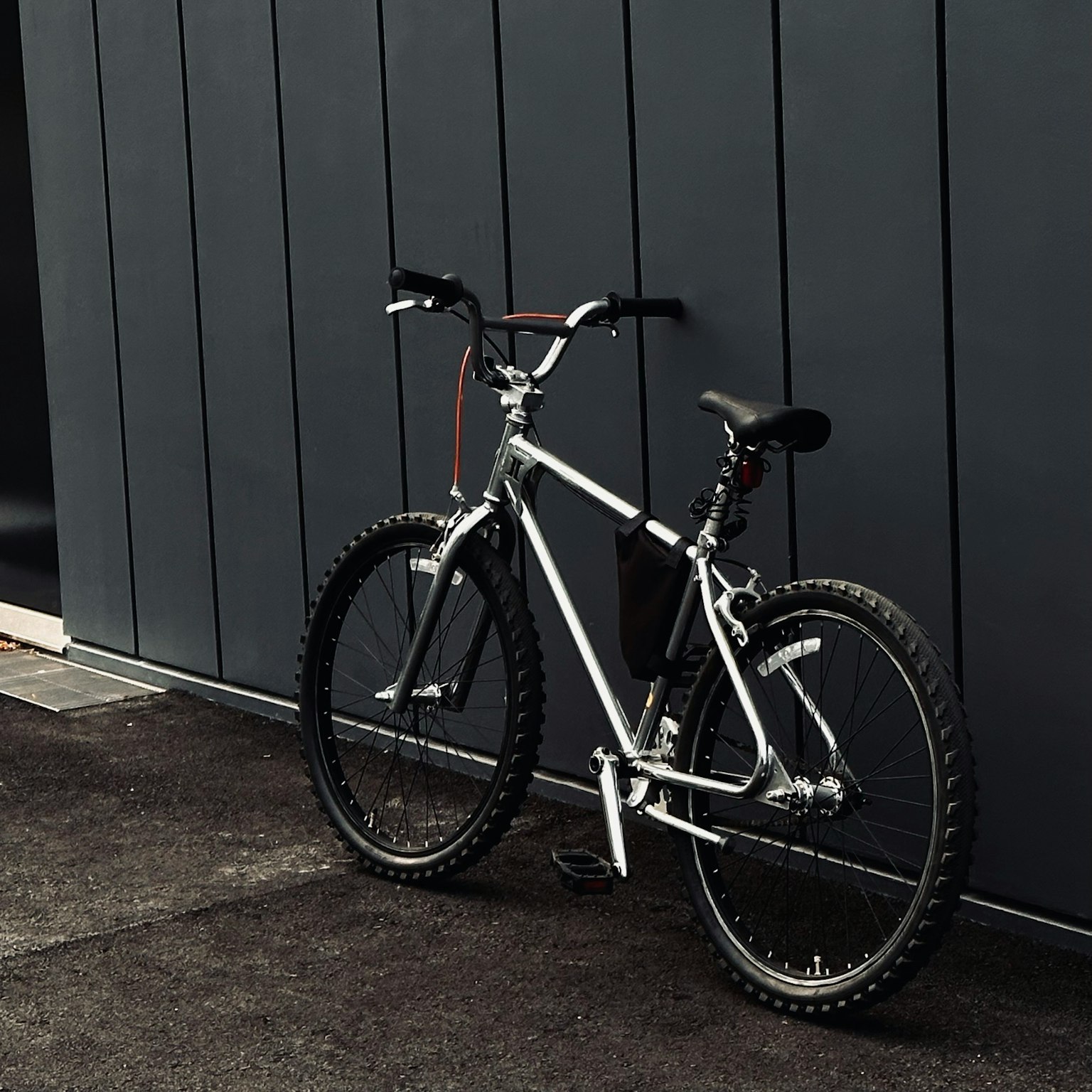 Ein elegantes silbernes Mountainbike lehnt an einer dunklen Wand