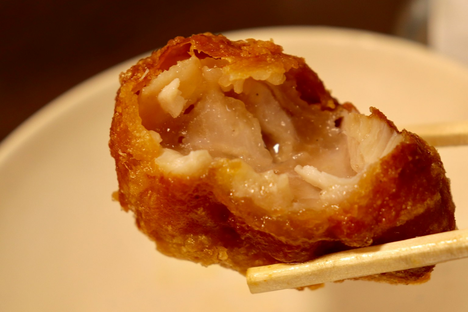 Primer plano de un trozo de pollo frito sostenido por palillos