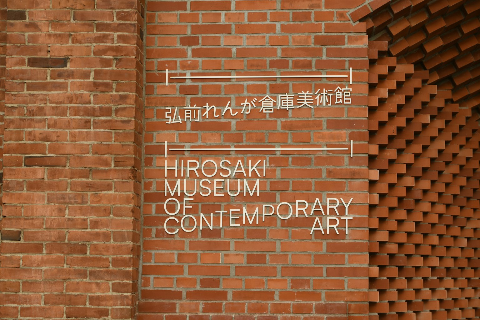 Biển chỉ dẫn Bảo tàng Nghệ thuật Đương đại Hirosaki trên tường gạch