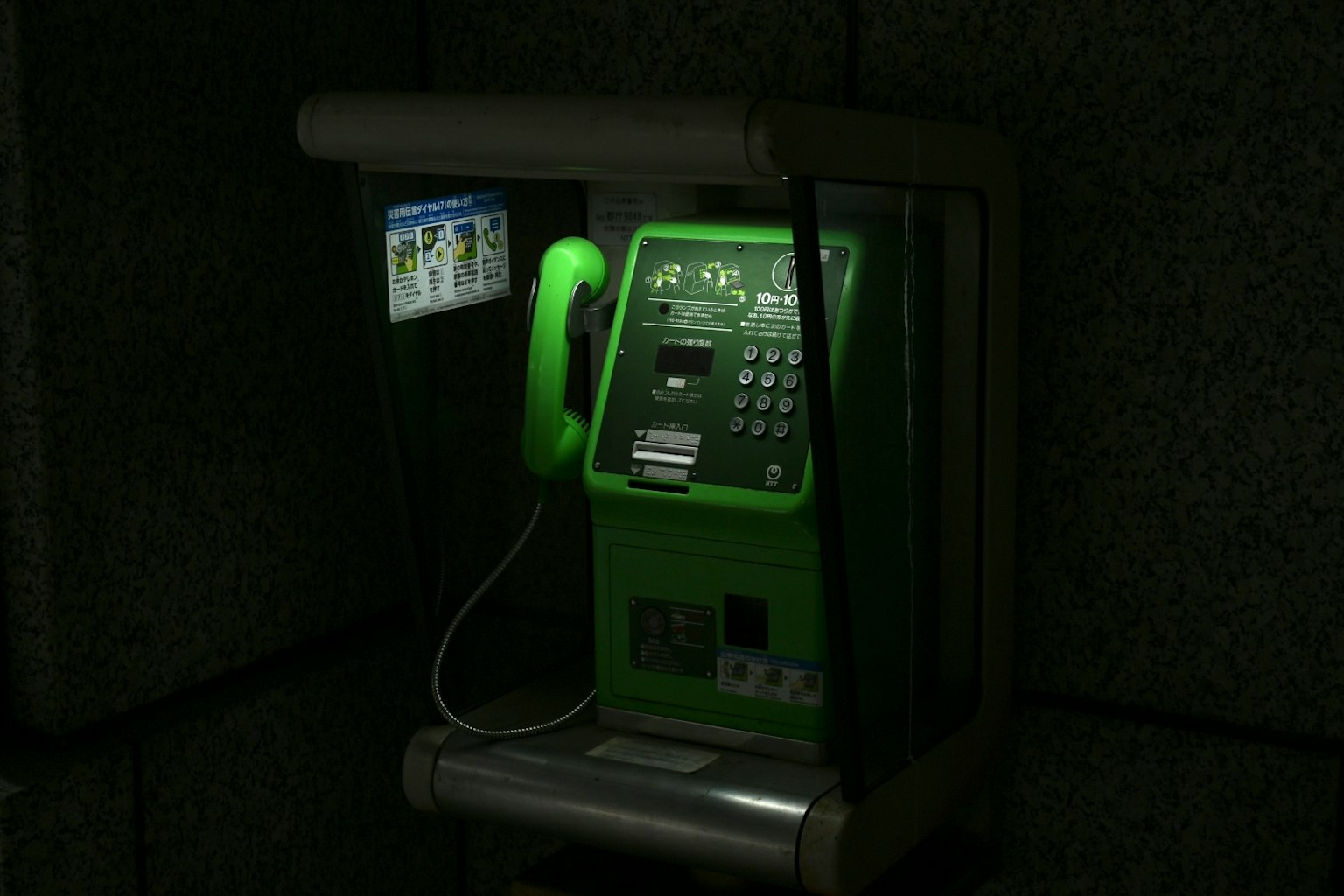 Cabine téléphonique publique verte installée sur un fond sombre