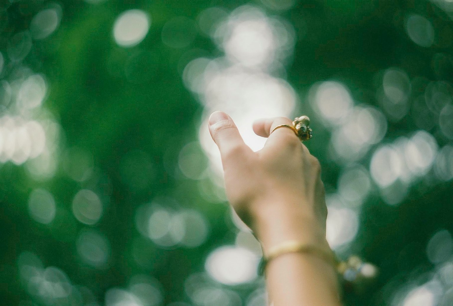A hand reaching upwards against a green blurred background featuring several rings