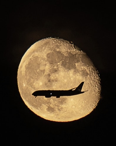 An airplane silhouette against an autumn full moon night sky