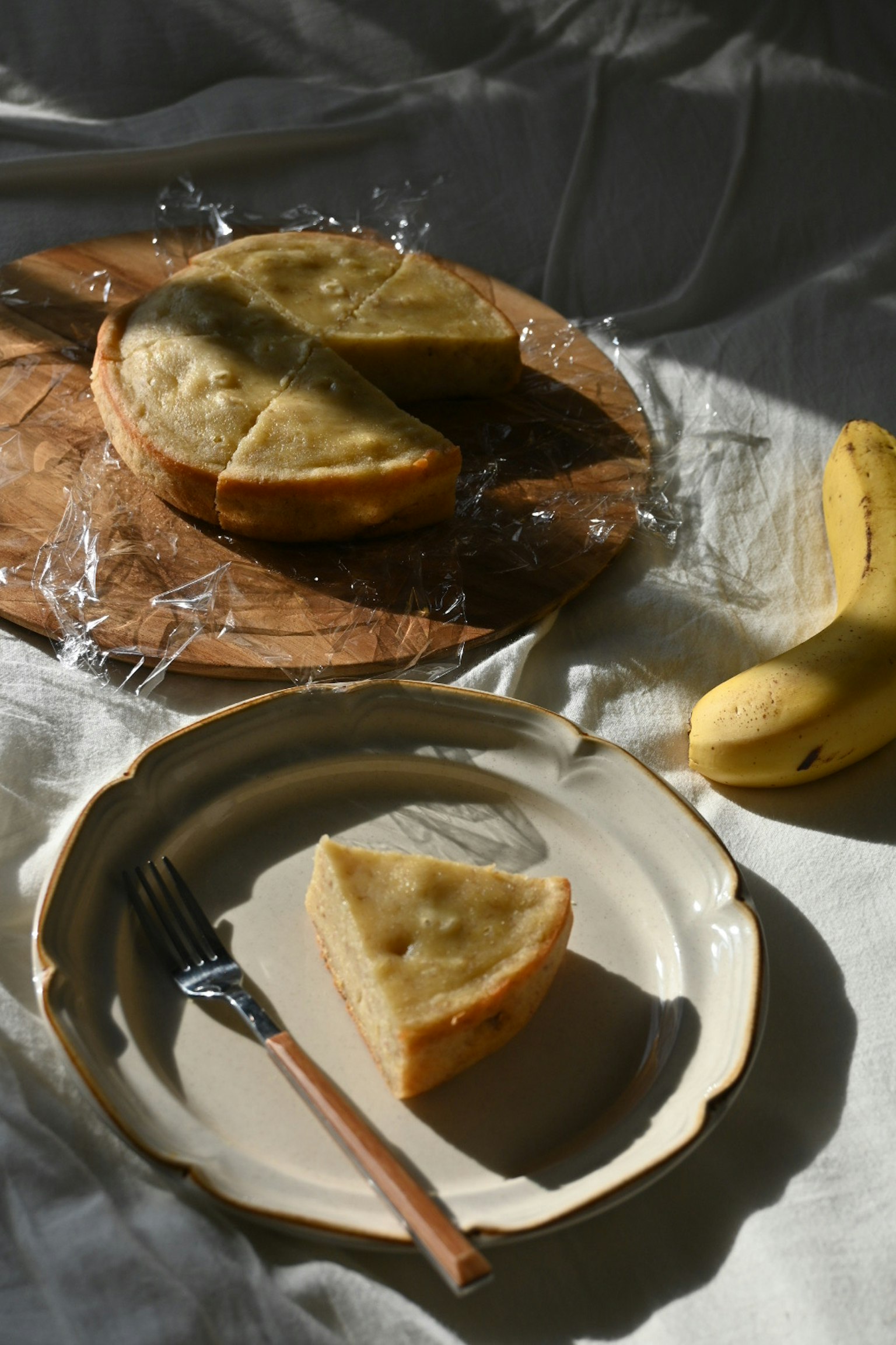Geschnittene Bananentorte auf einem Holzbrett mit einer Banane daneben