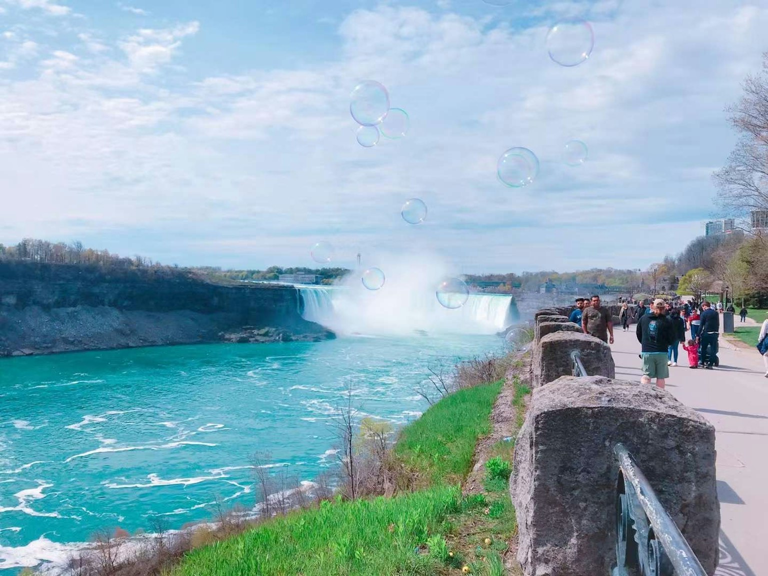 Orang-orang berjalan di sepanjang jalan dengan pemandangan Air Terjun Niagara dan air berwarna turquoise