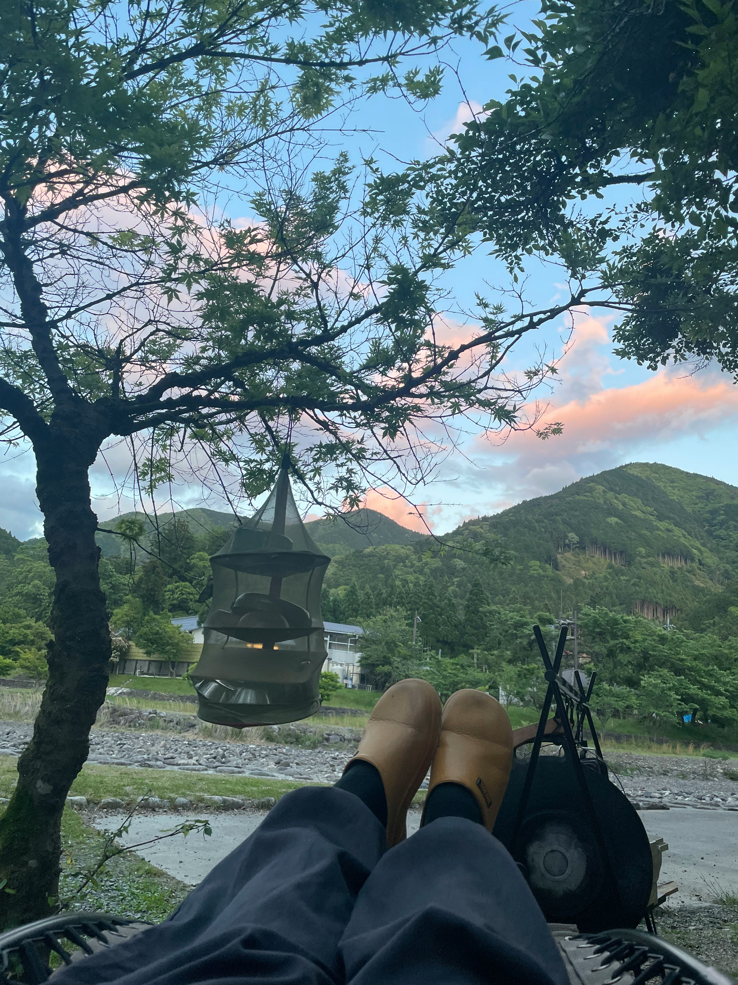 川辺のキャンプ場で焚き火台とランタン、山並みを眺める景色