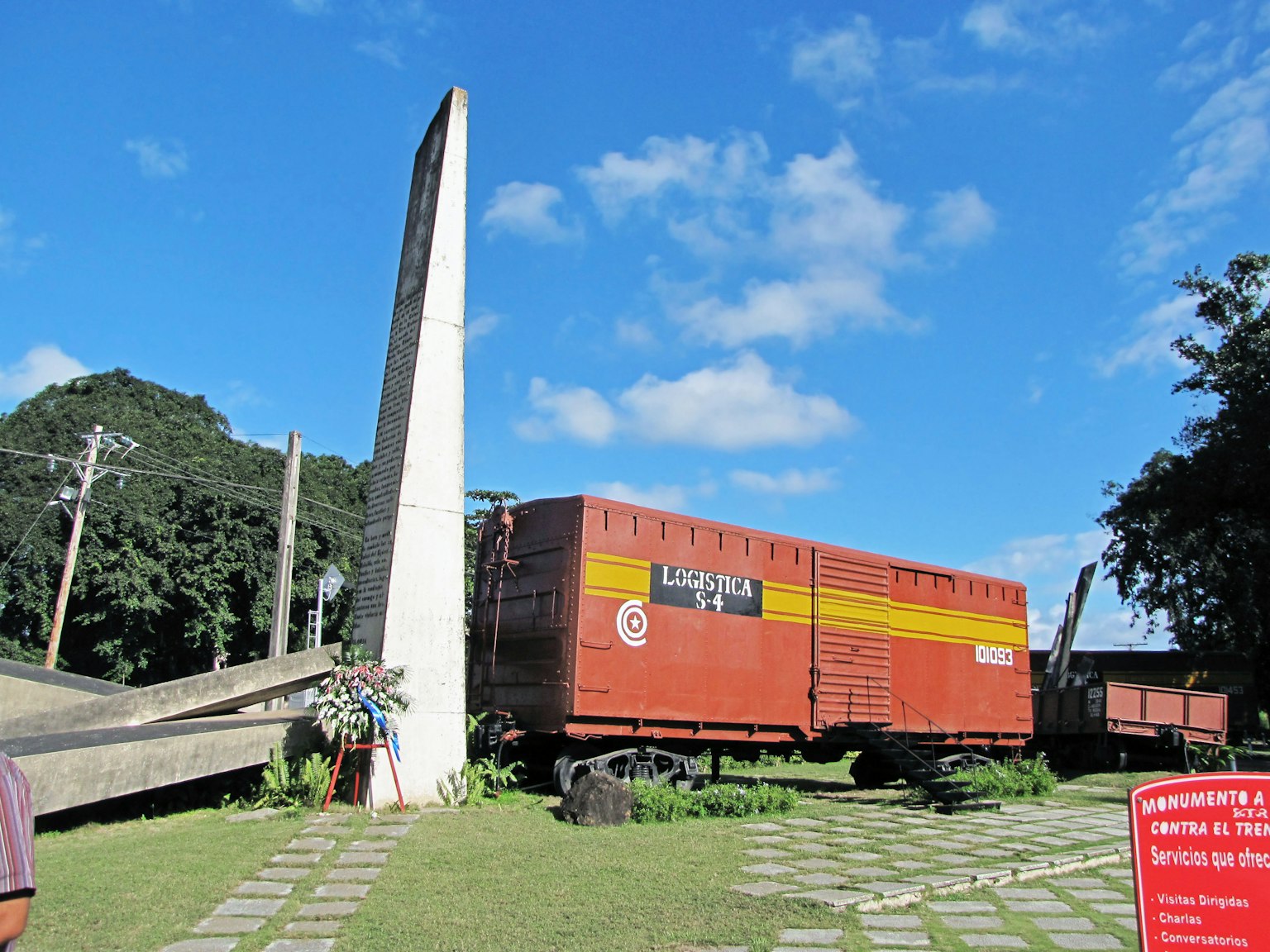 Un vagón de tren de carga rojo junto a un monumento alto bajo un cielo azul