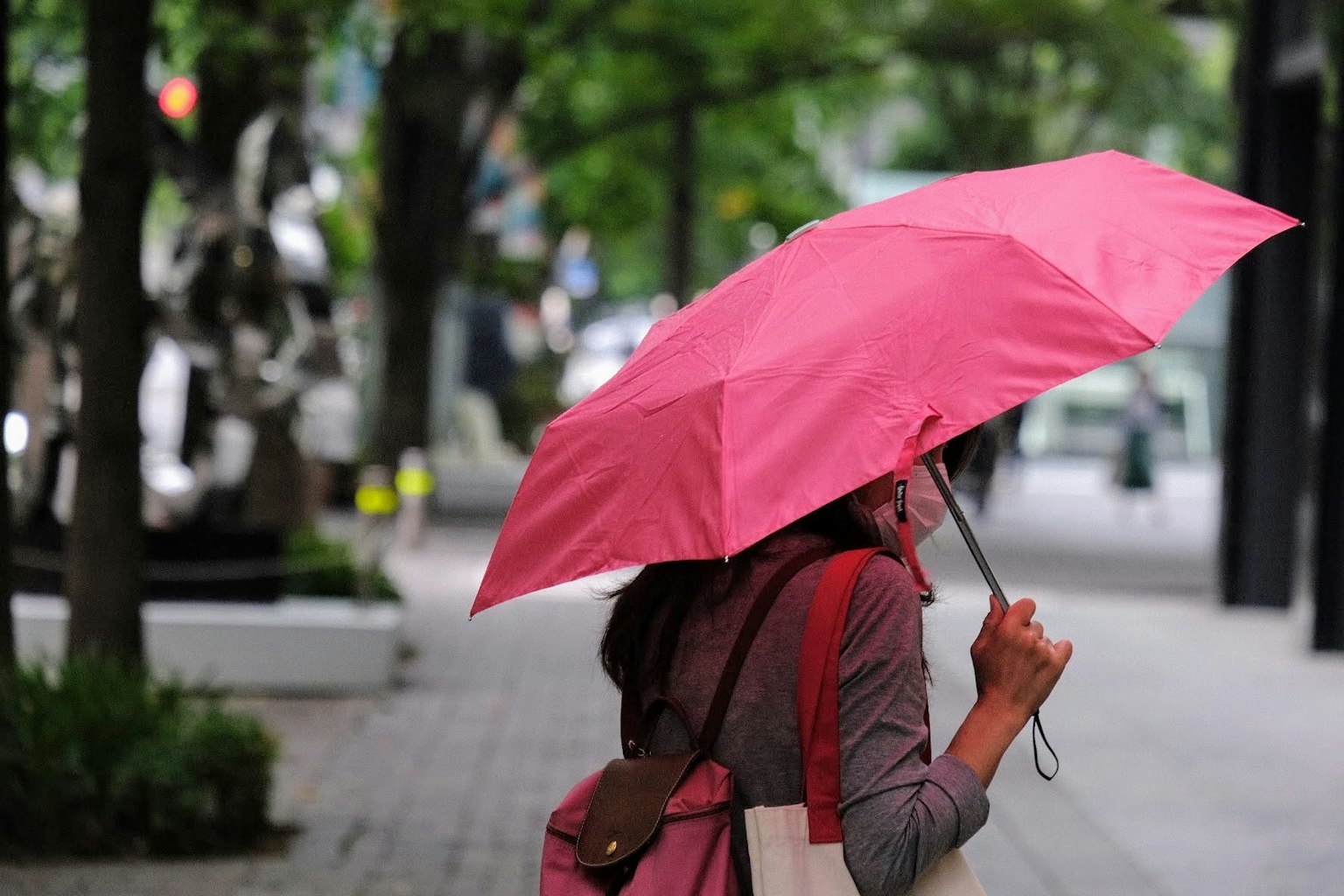 Una mujer caminando por la calle con un paraguas rosa