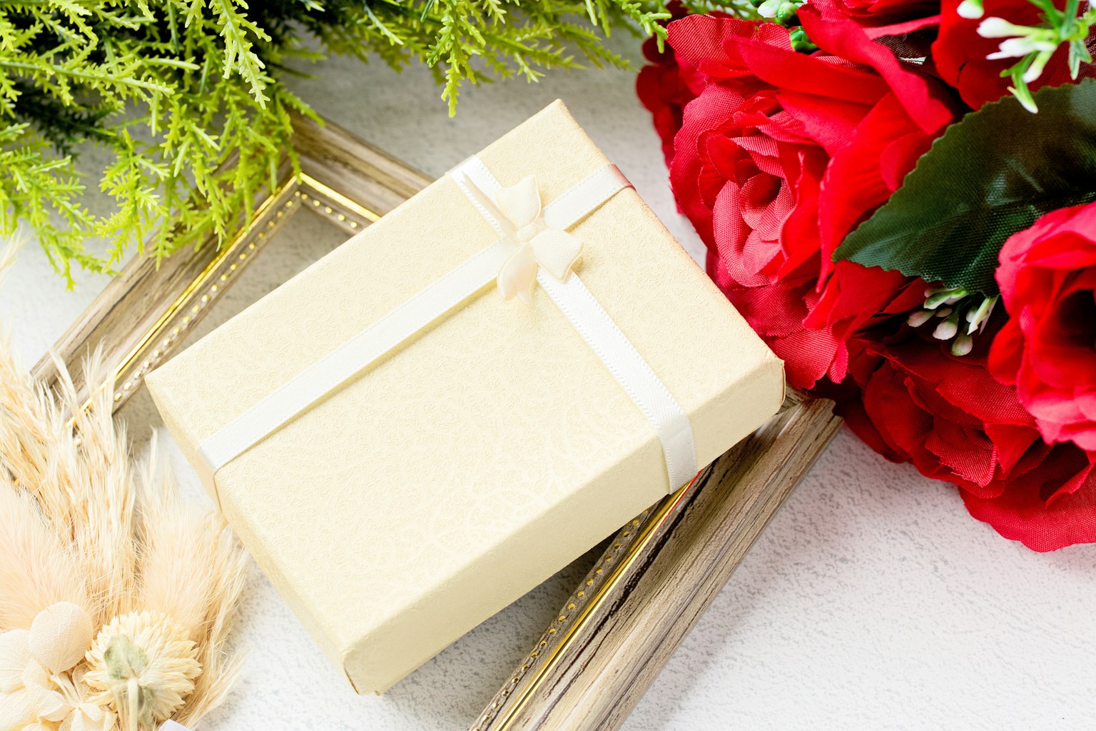 Scatola regalo color crema circondata da rose rosse e foglie verdi