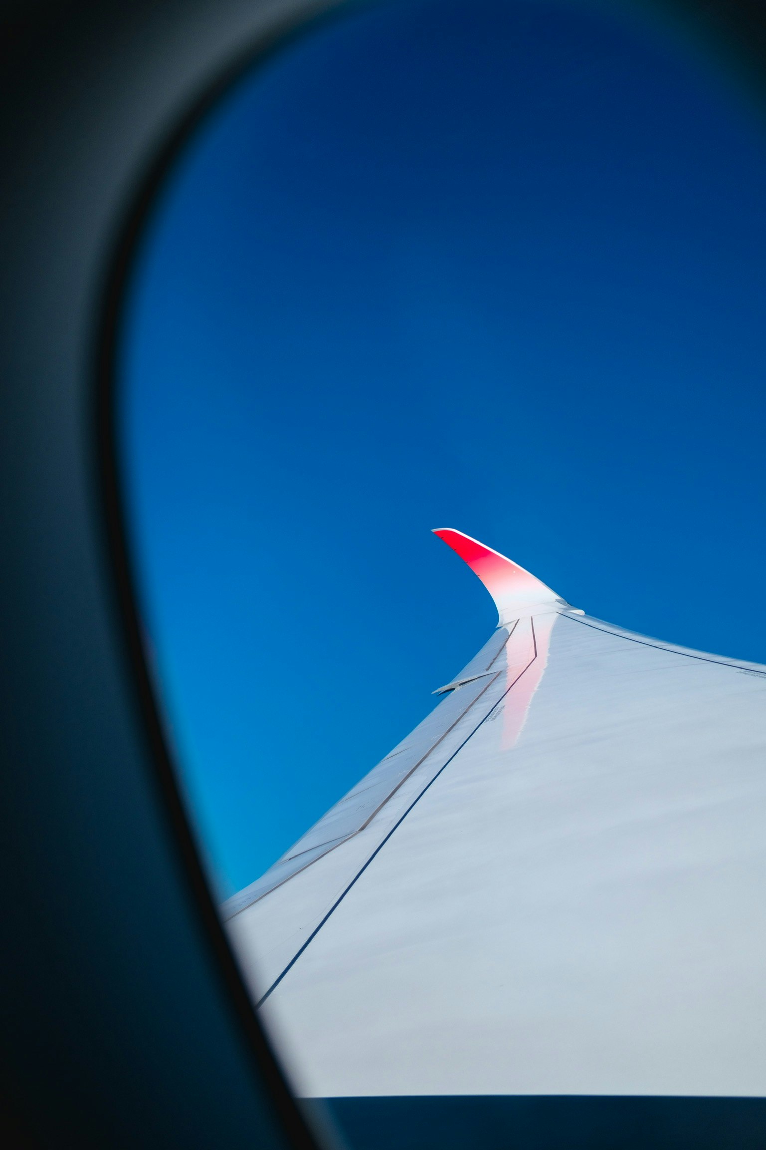 Airplane wing tip with red accent against blue sky
