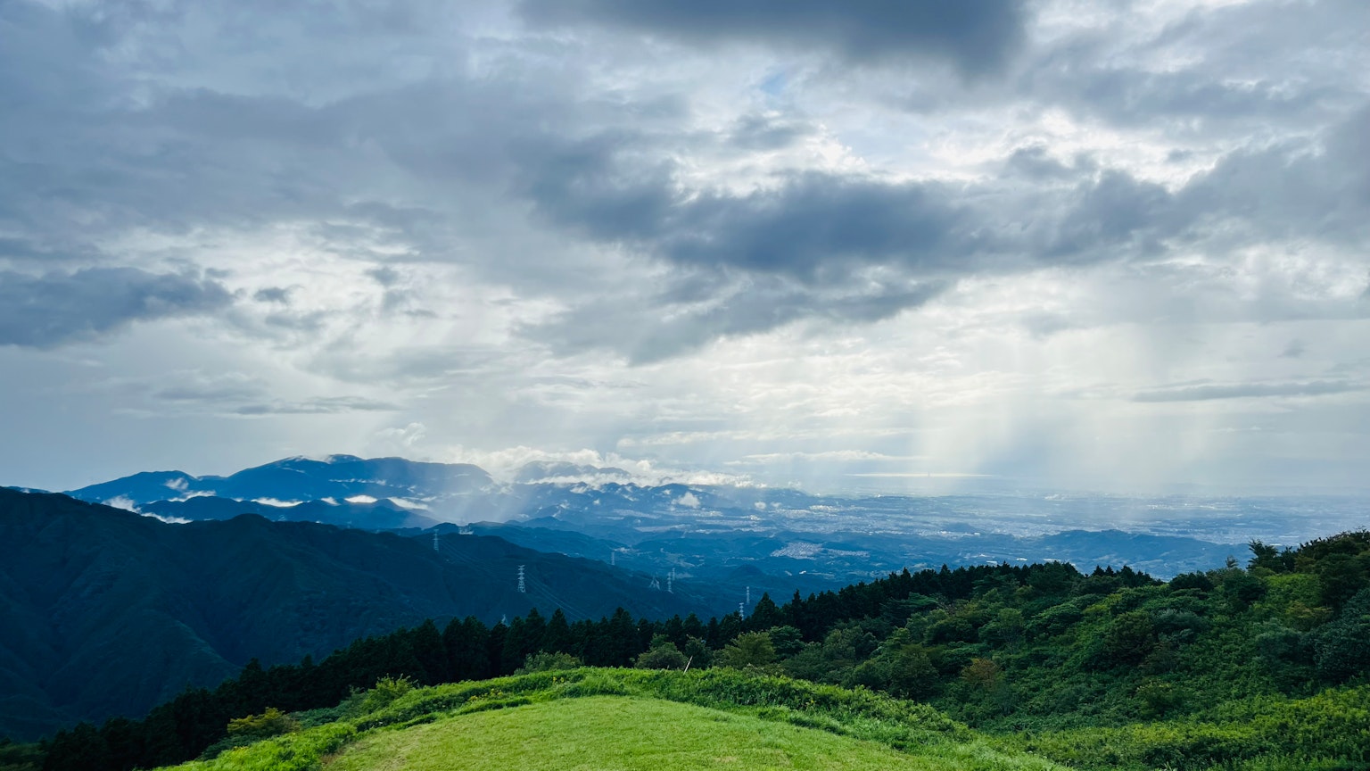 Vue panoramique de collines vertes et de montagnes sous un ciel nuageux