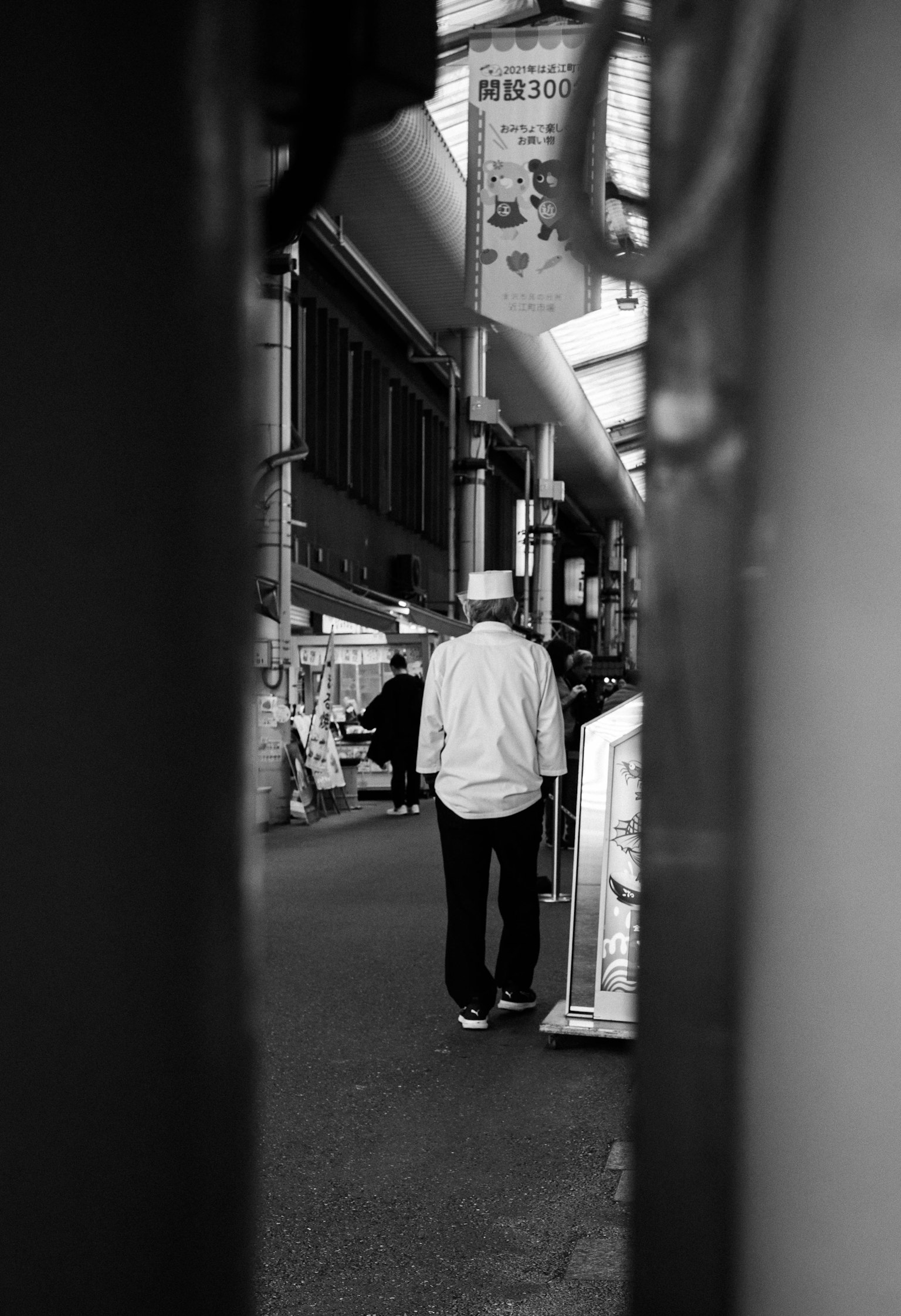 Un hombre con chaqueta blanca caminando por una calle estrecha capturada en blanco y negro