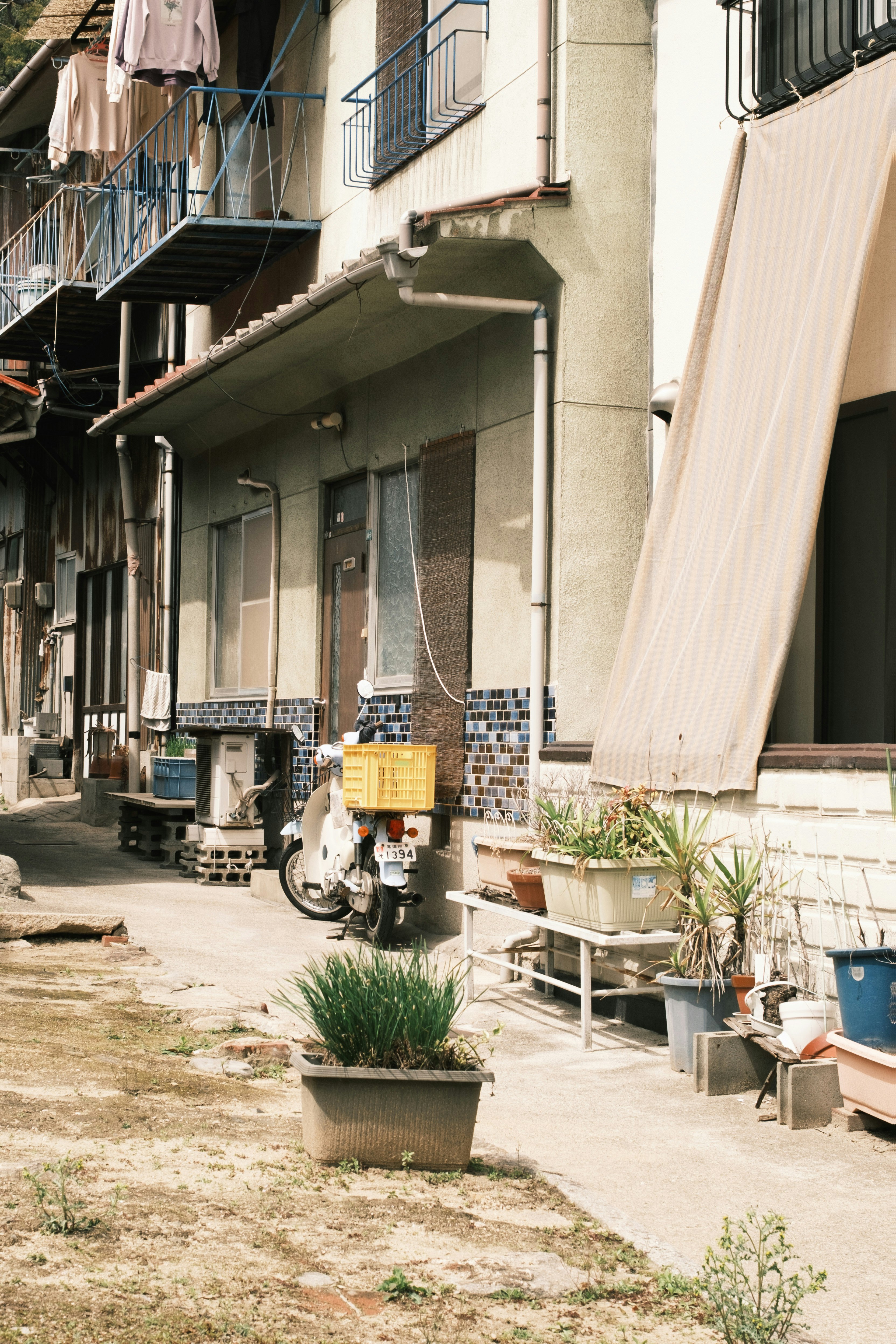 路地の軒先に並ぶ自転車と鉢植えのある商店街の建物