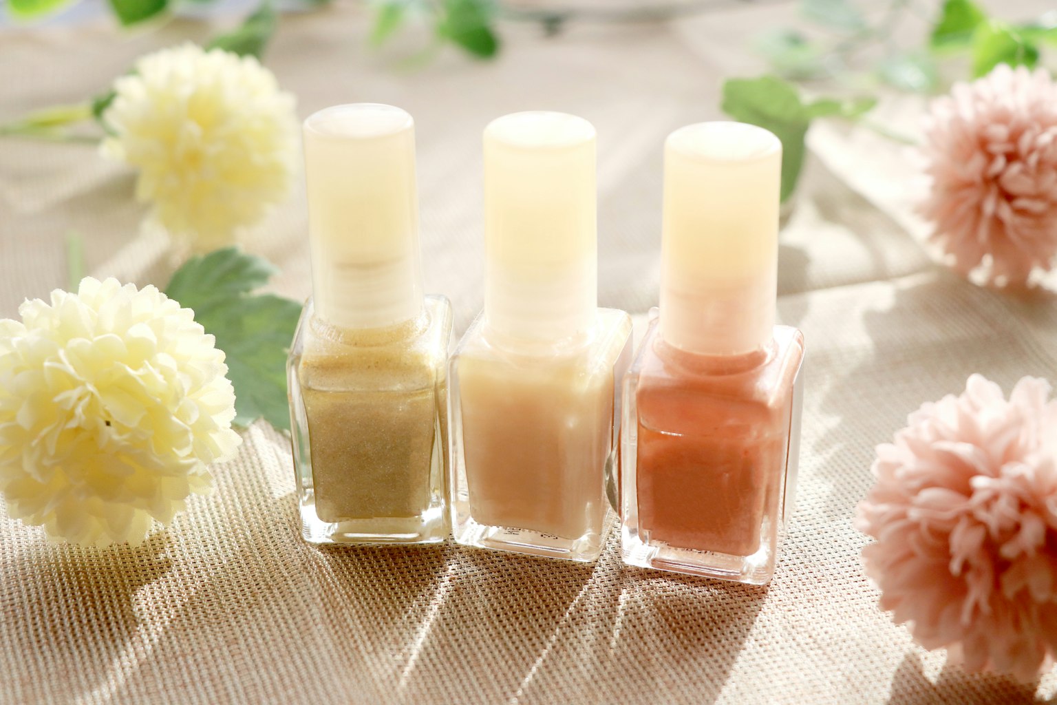 ภาพของยาทาเล็บสีธรรมชาติที่จัดเรียงพร้อมกับดอกไม้ที่นุ่มนวลในพื้นหลัง