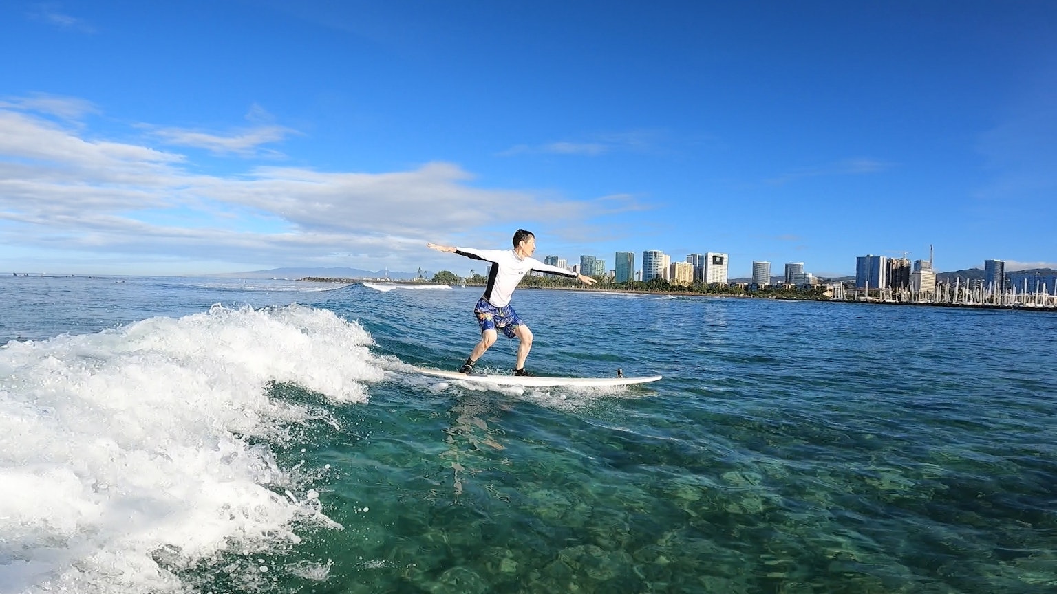 Un uomo che fa surf su una tavola cavalcando un'onda sotto un cielo blu chiaro