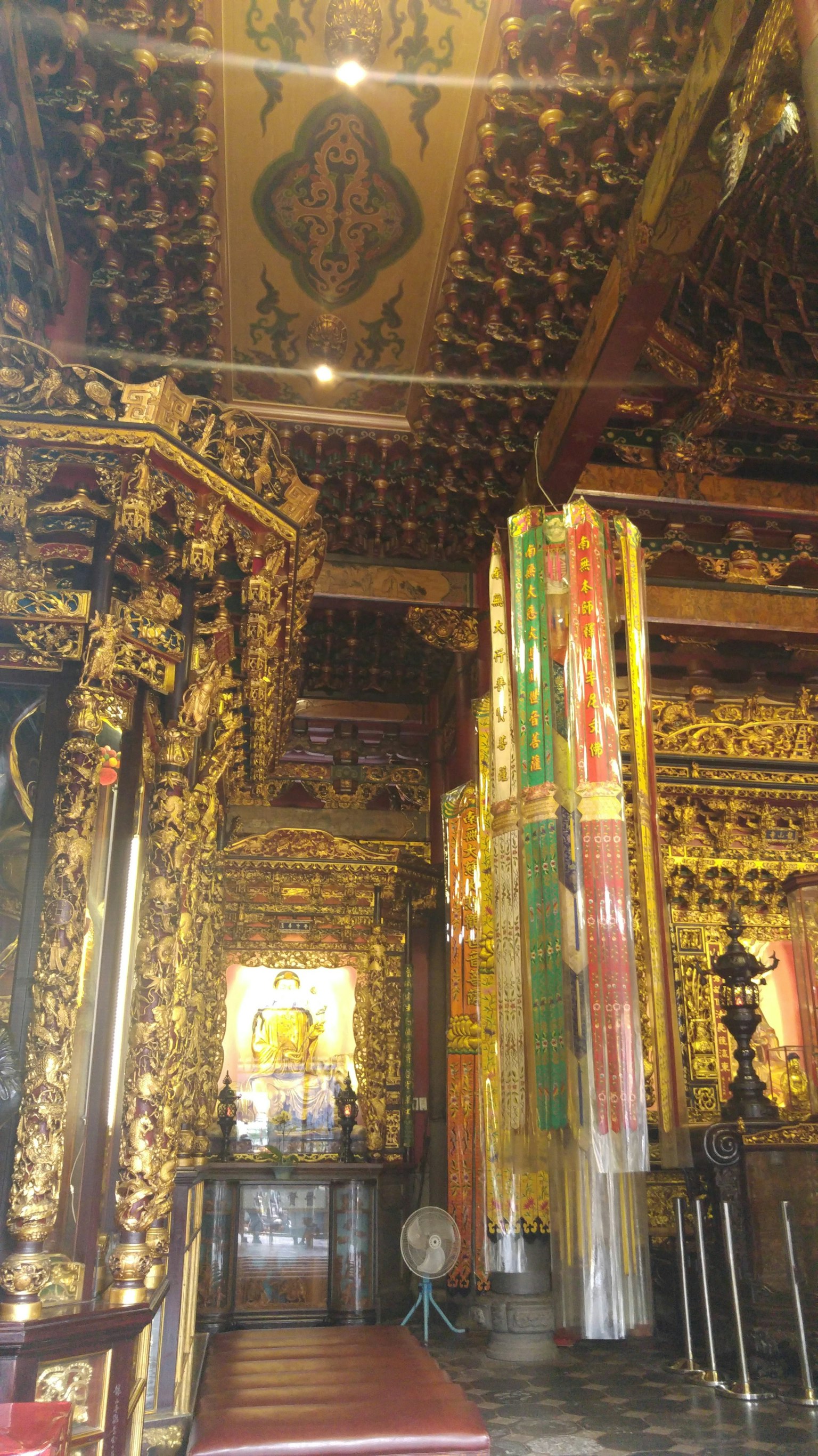 Interior of a richly decorated temple featuring golden carvings on walls and ceiling colorful banners hanging