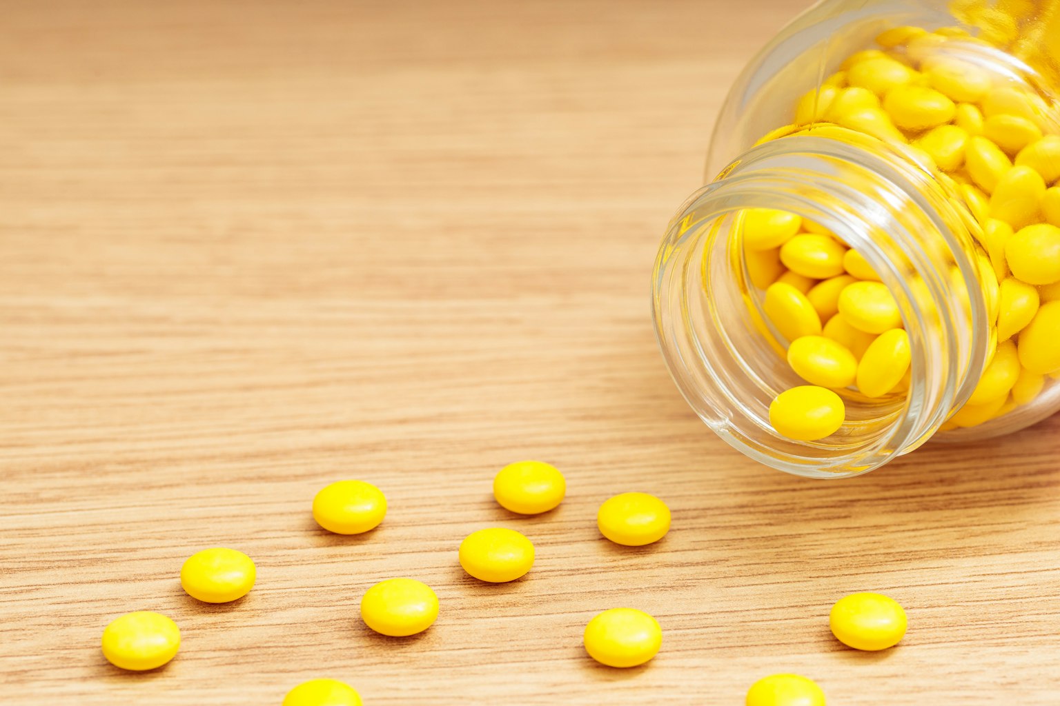 A jar of yellow round candies tipped over spilling some onto a wooden surface