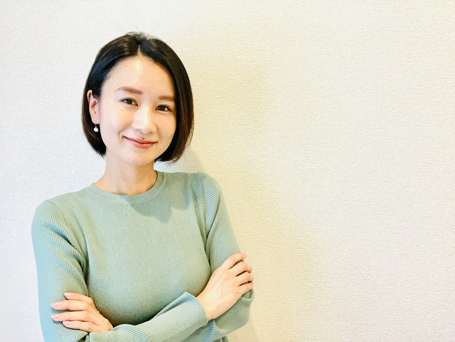 一位微笑的女性雙臂交叉站在淺色牆前
