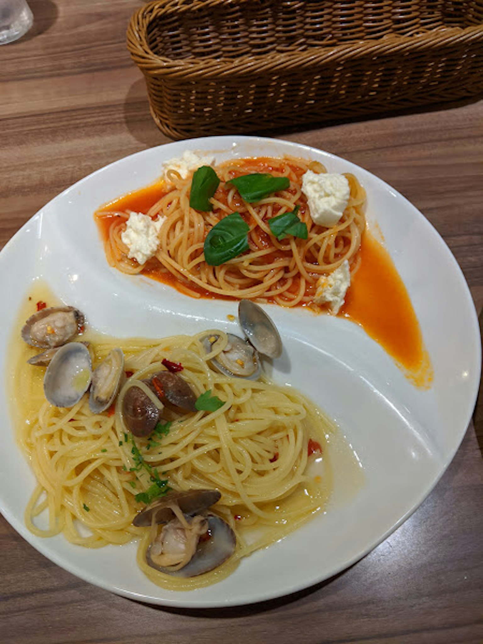 Hai đĩa pasta trên đĩa trắng, đĩa trên với sốt cà chua và húng quế, đĩa dưới với ngao và dầu ô liu