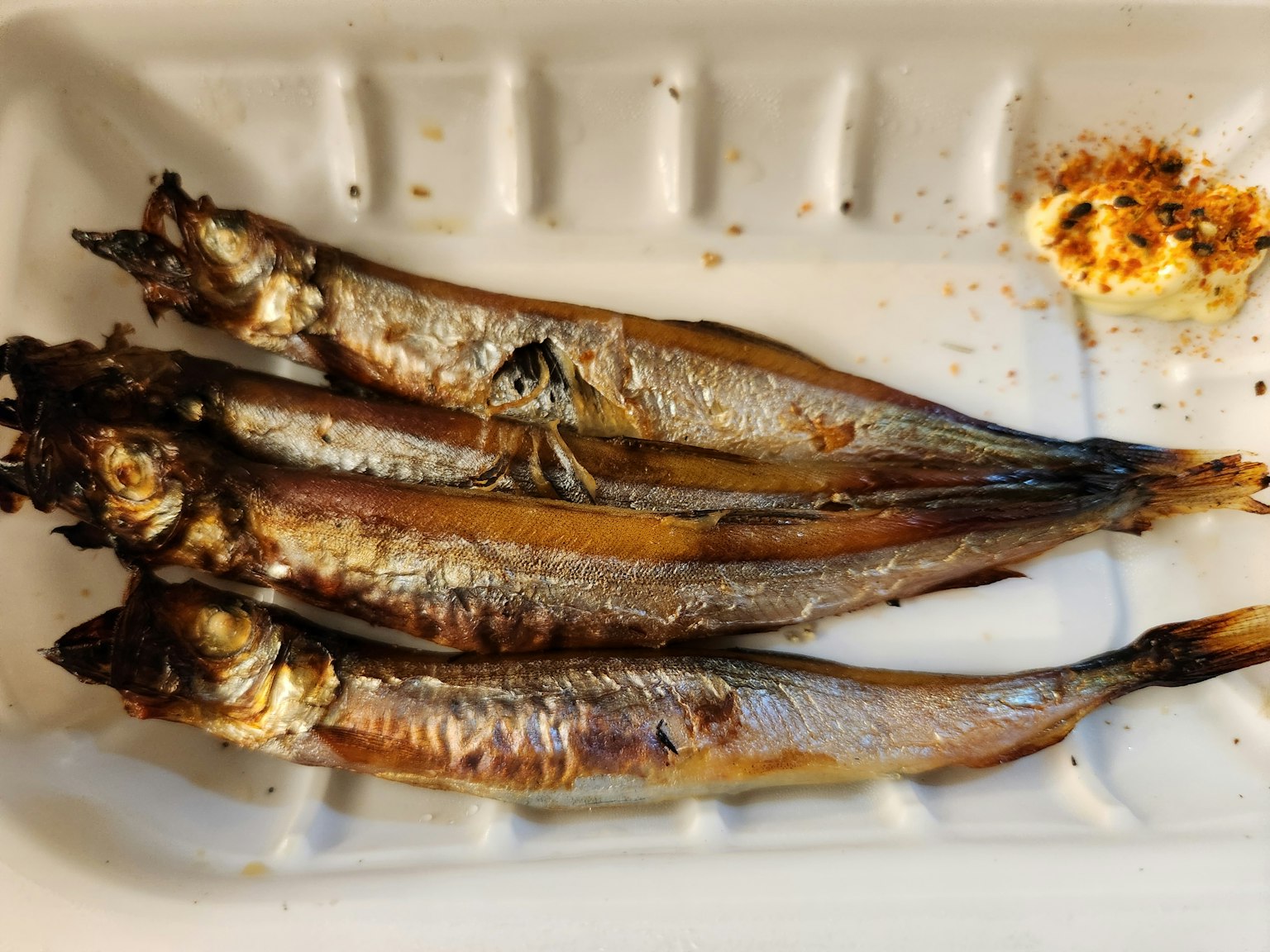 Vier gegrillte kleine Fische auf einem Teller mit einer knusprigen Beilage