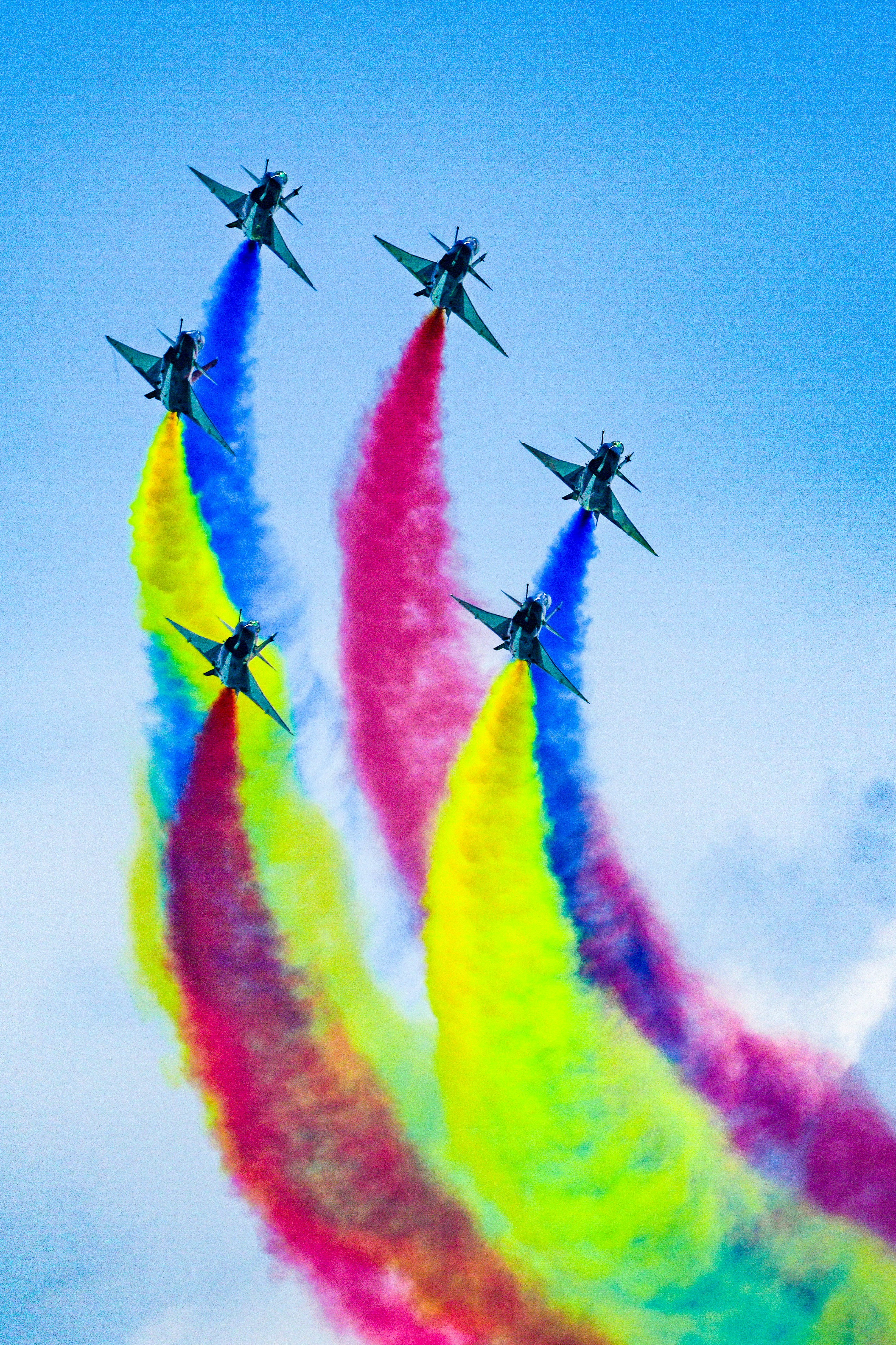 青空の下でカラフルな煙を描く曲技飛行のジェット機