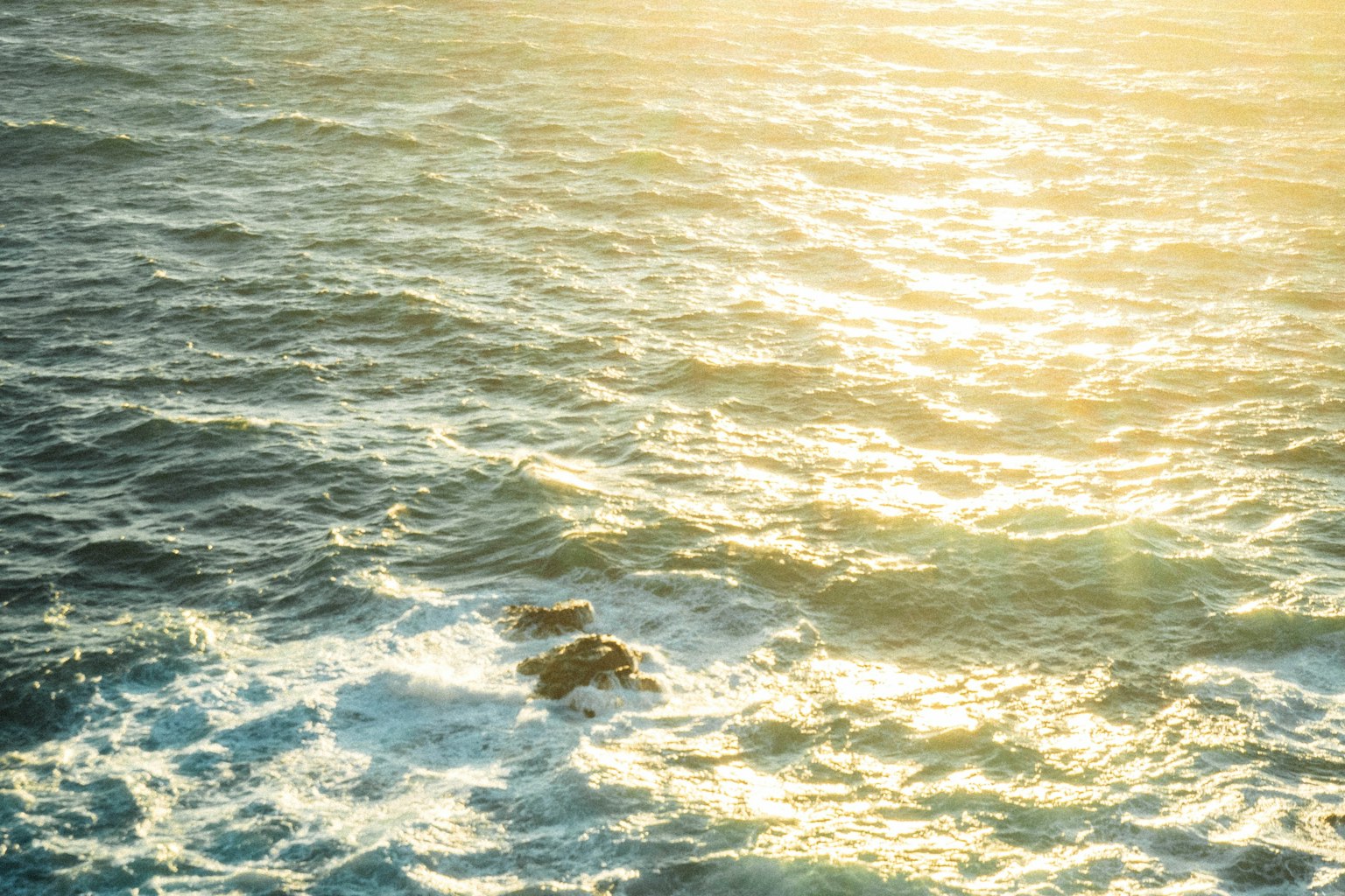 Luz del sol brillando en las olas del océano con rocas visibles